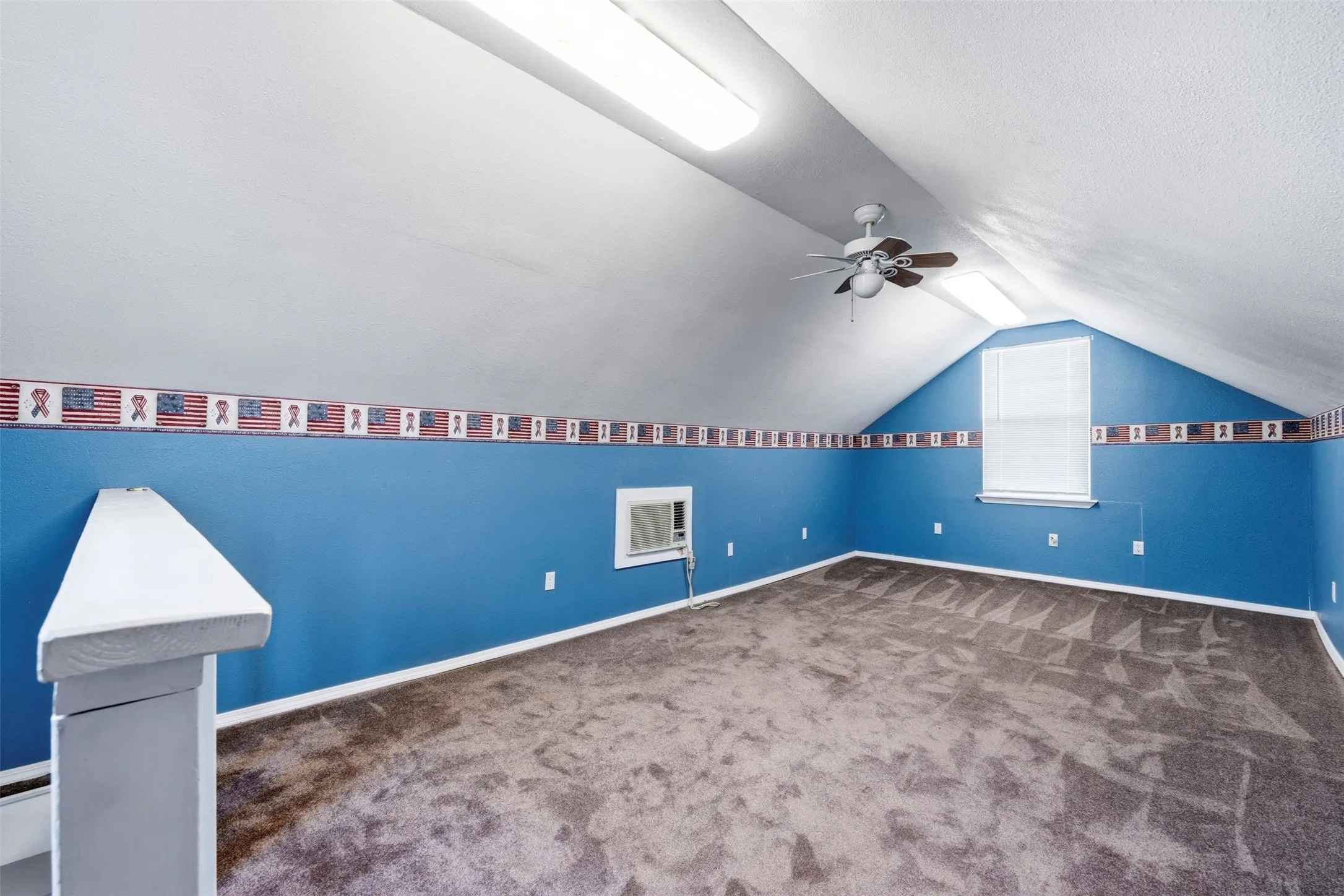 Carpeted room with sloped ceilings, ceiling fan, window with blinds, and wall-mounted air conditioning unit