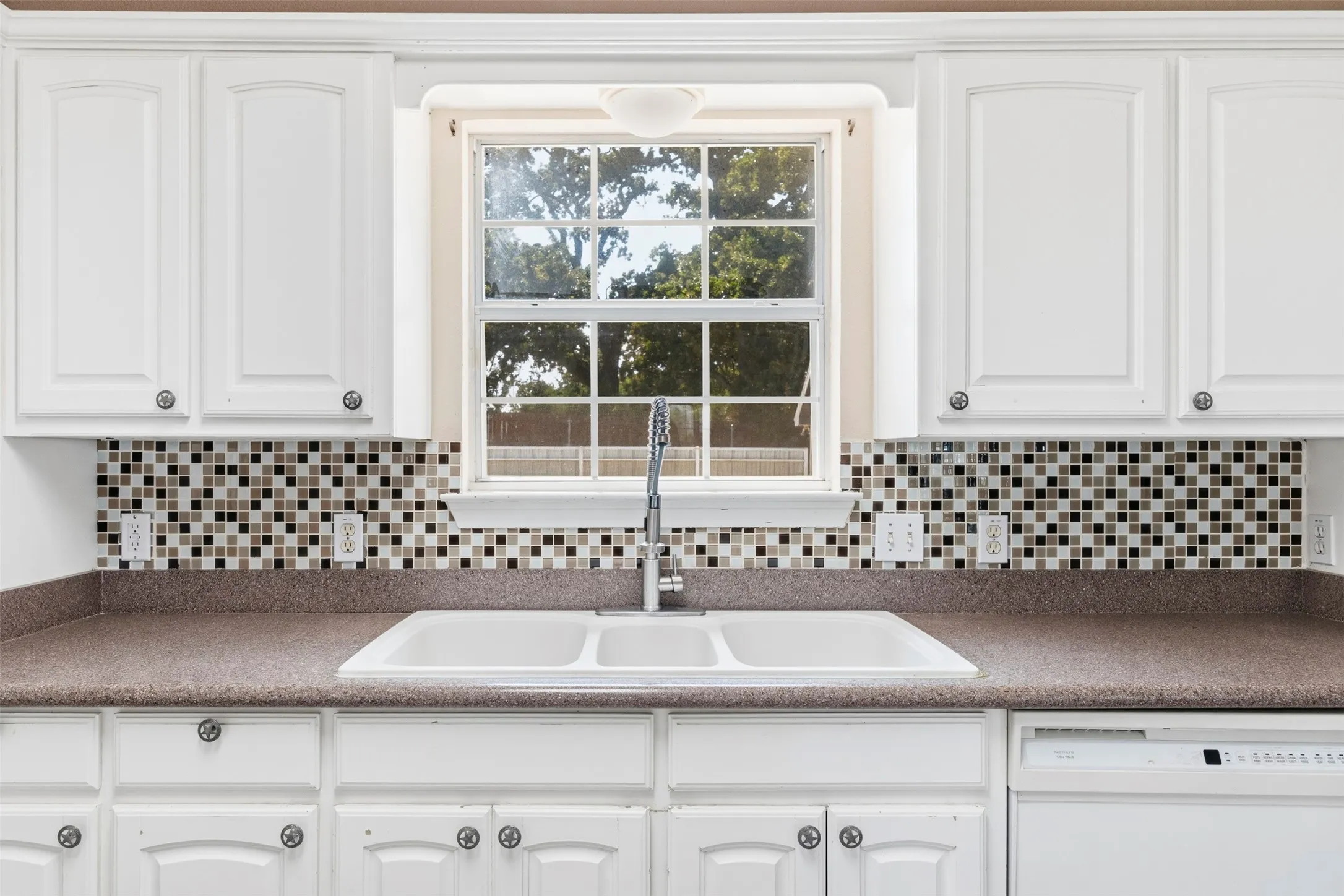 White cabinetry with decorative pulls, mosaic tile backsplash, double basin sink with a gooseneck faucet, and a built-in dishwasher
