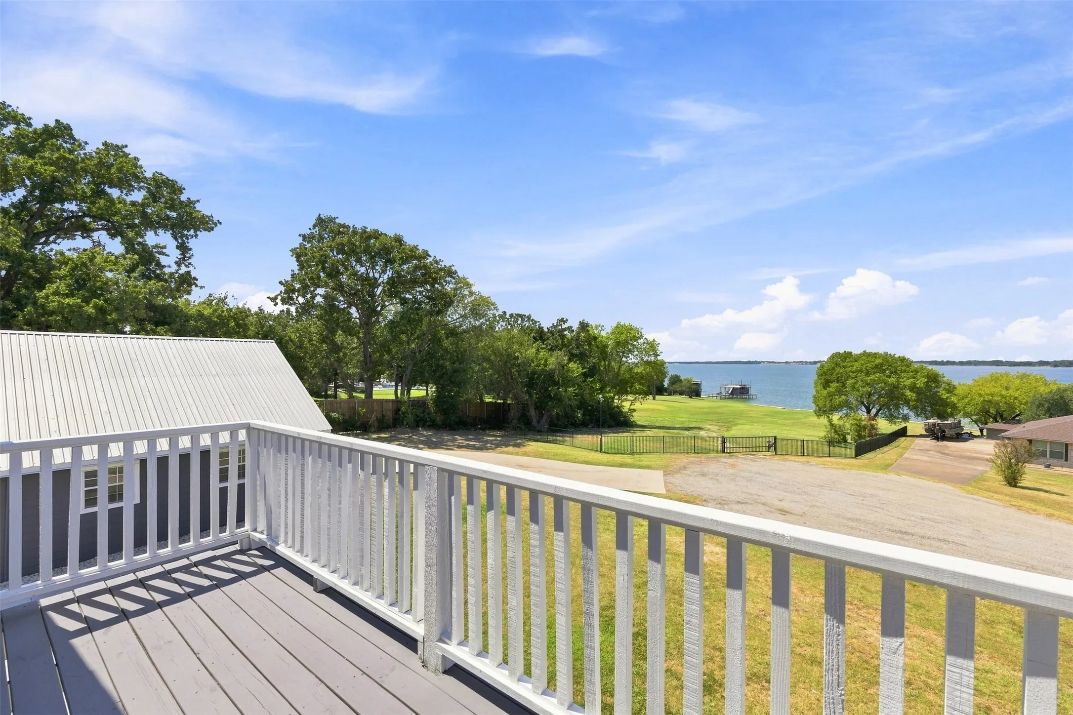 Upper-level deck with wood-finish flooring and white railing with view of the lake