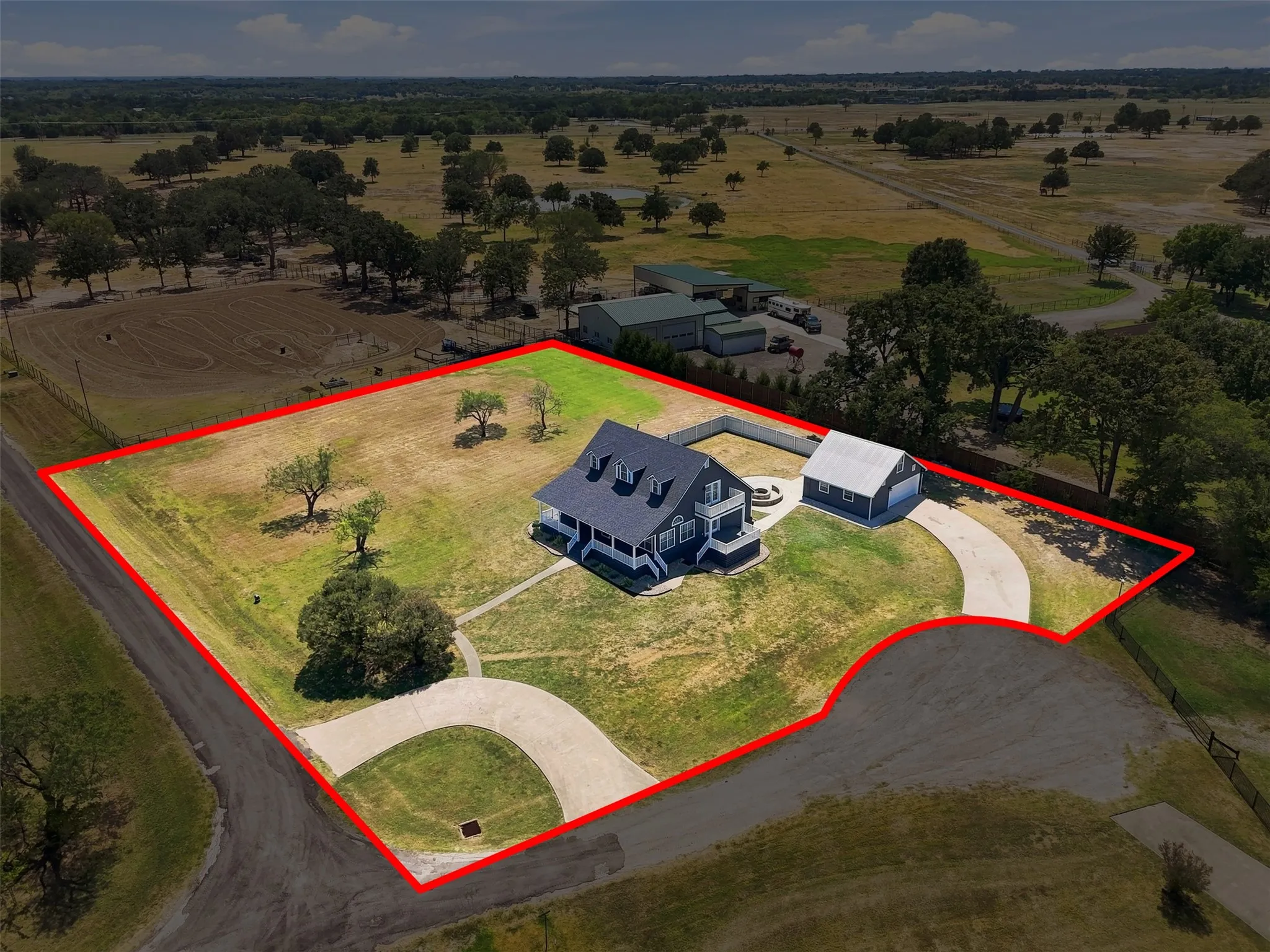 Two-story residence with a dark roof and light trim, detached garage with a light roof, expansive lot with mature trees, and a paved driveway