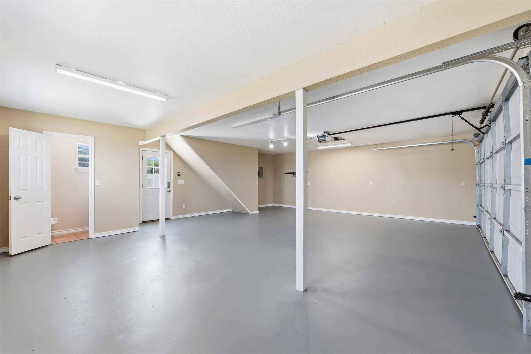 Spacious garage with a finished floor, multiple fluorescent light fixtures, an overhead garage door, and a dedicated utility area