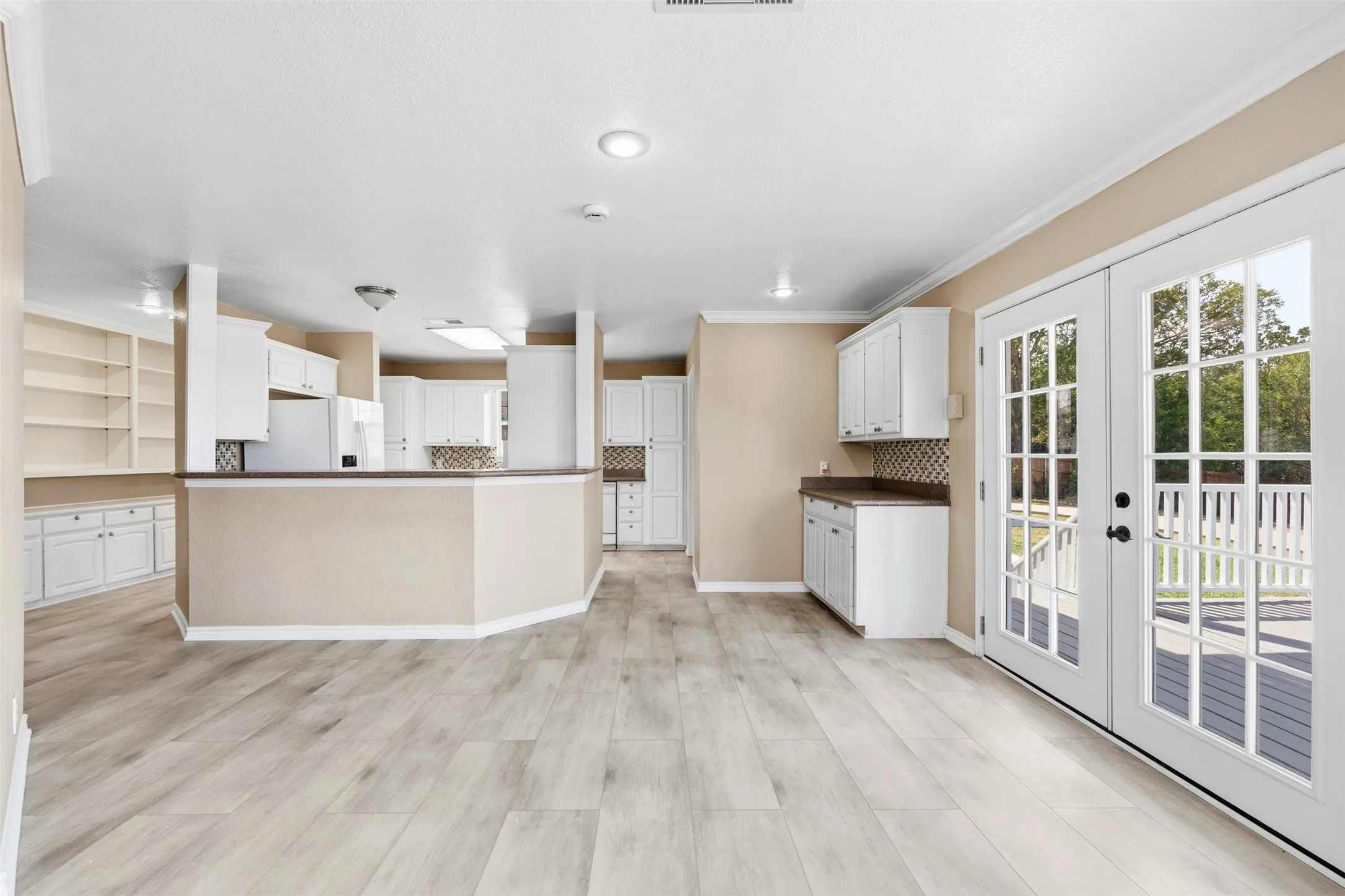 Light wood-finish flooring, built-in shelving, white cabinetry, French doors, and a deck
