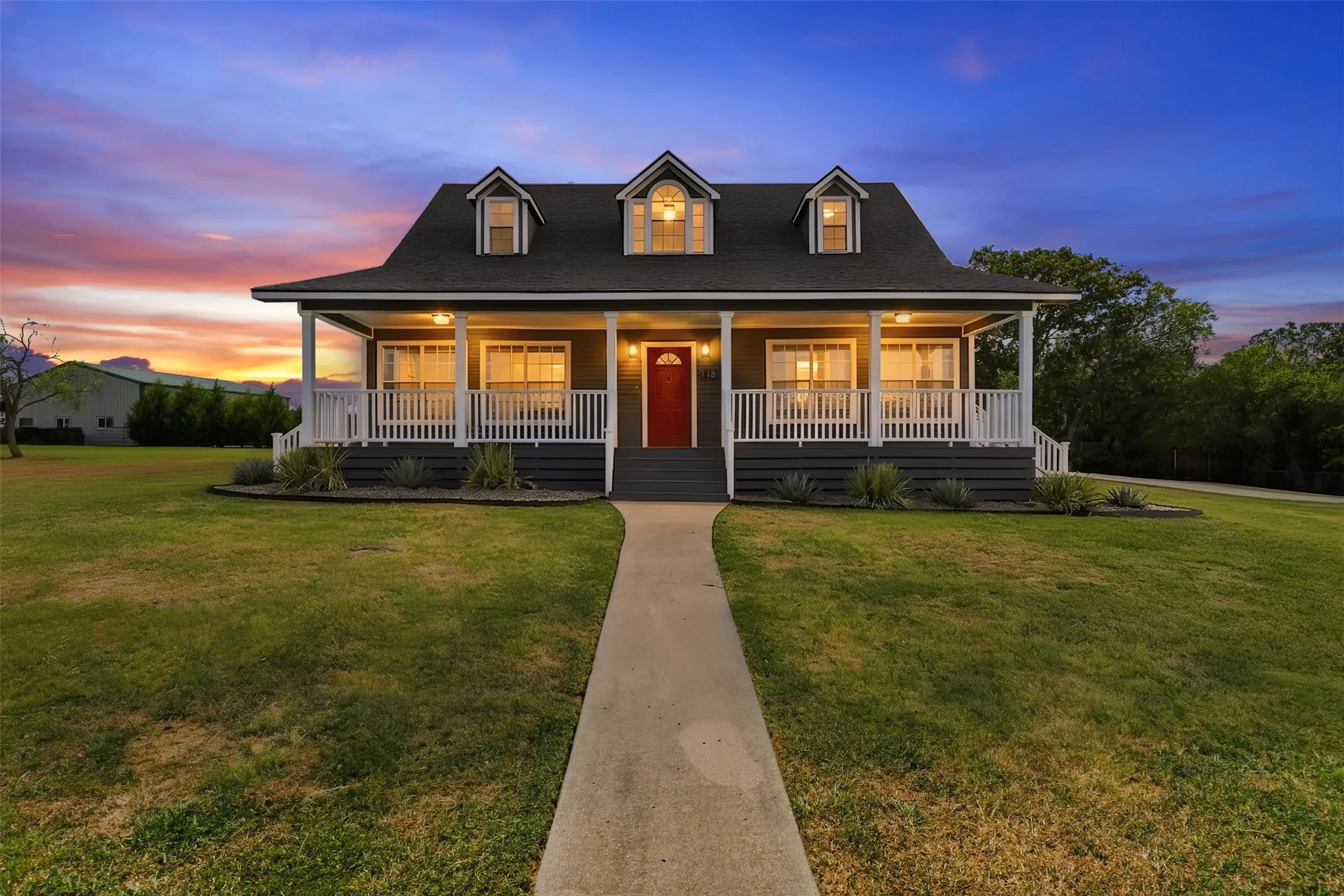 Two-story residence with dormer windows, a full-width covered front porch with white railings, and a bold red entry door