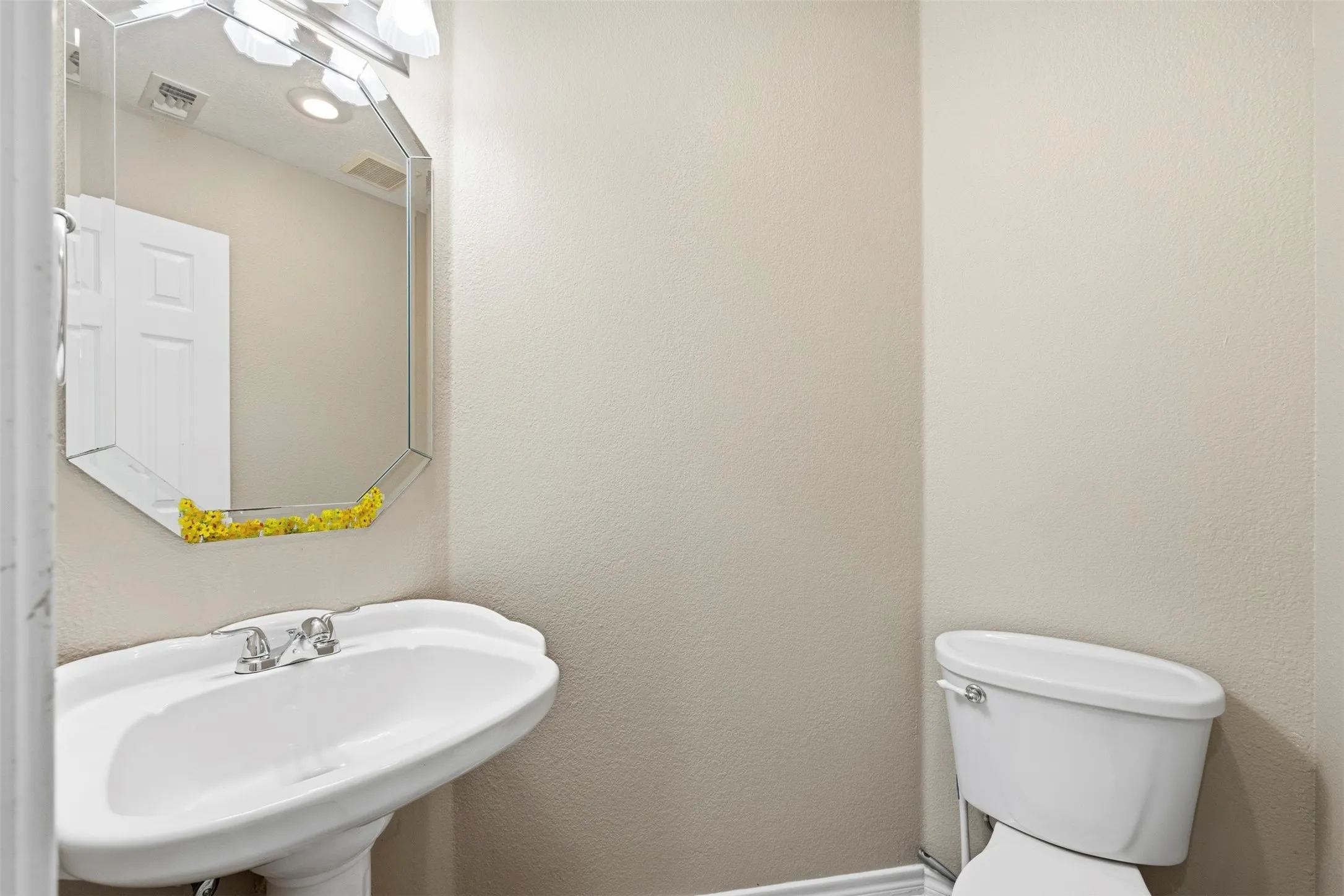 Pedestal sink with chrome fixtures, an octagonal wall mirror, and a wall-mounted light fixture