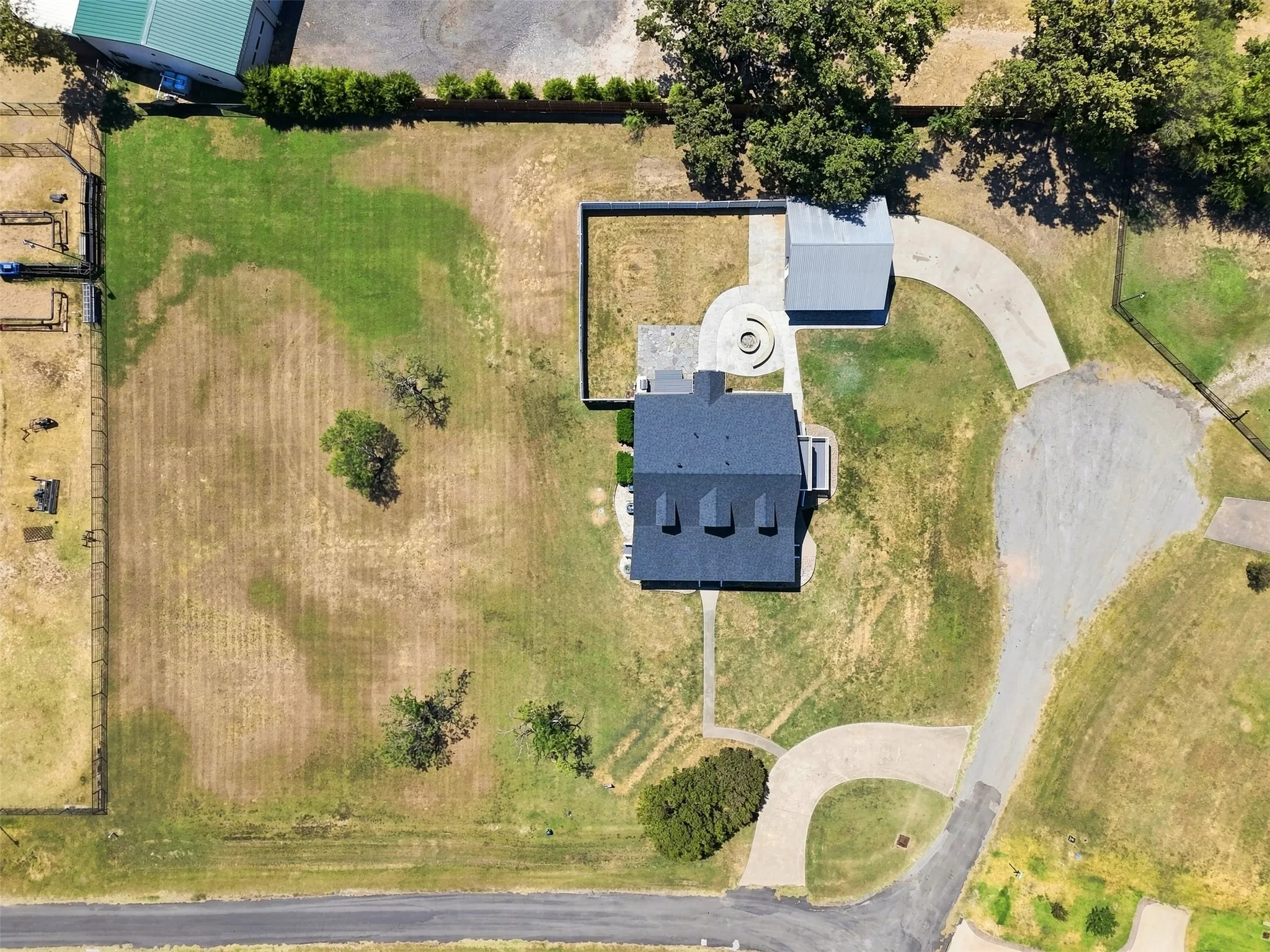 Expansive property featuring a main residence with a dark shingle roof, multiple dormer windows, a detached outbuilding, a circular driveway, and a fenced yard with mature trees