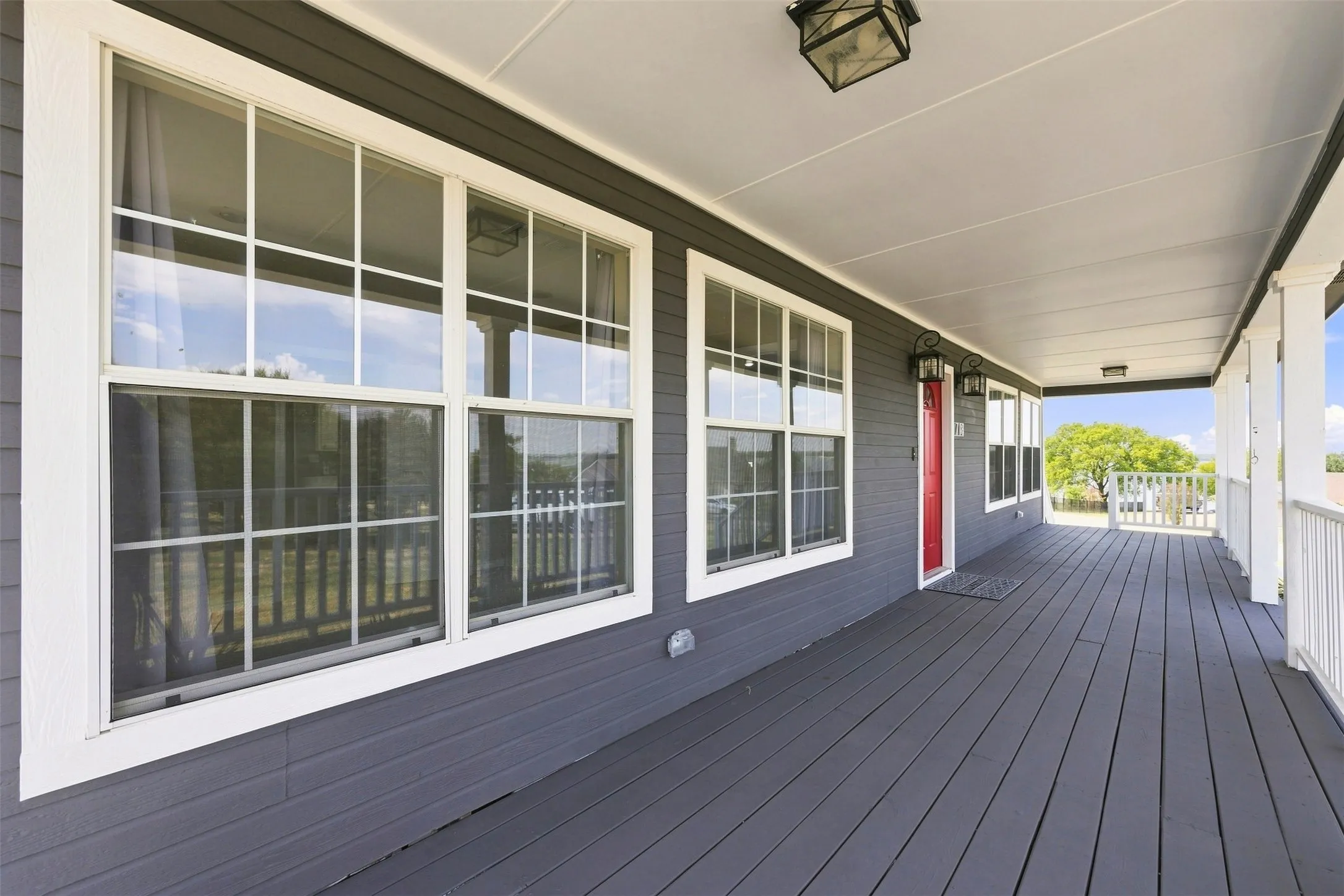 Expansive covered porch with dark wood-finish flooring, white columns, and a bright red entry door