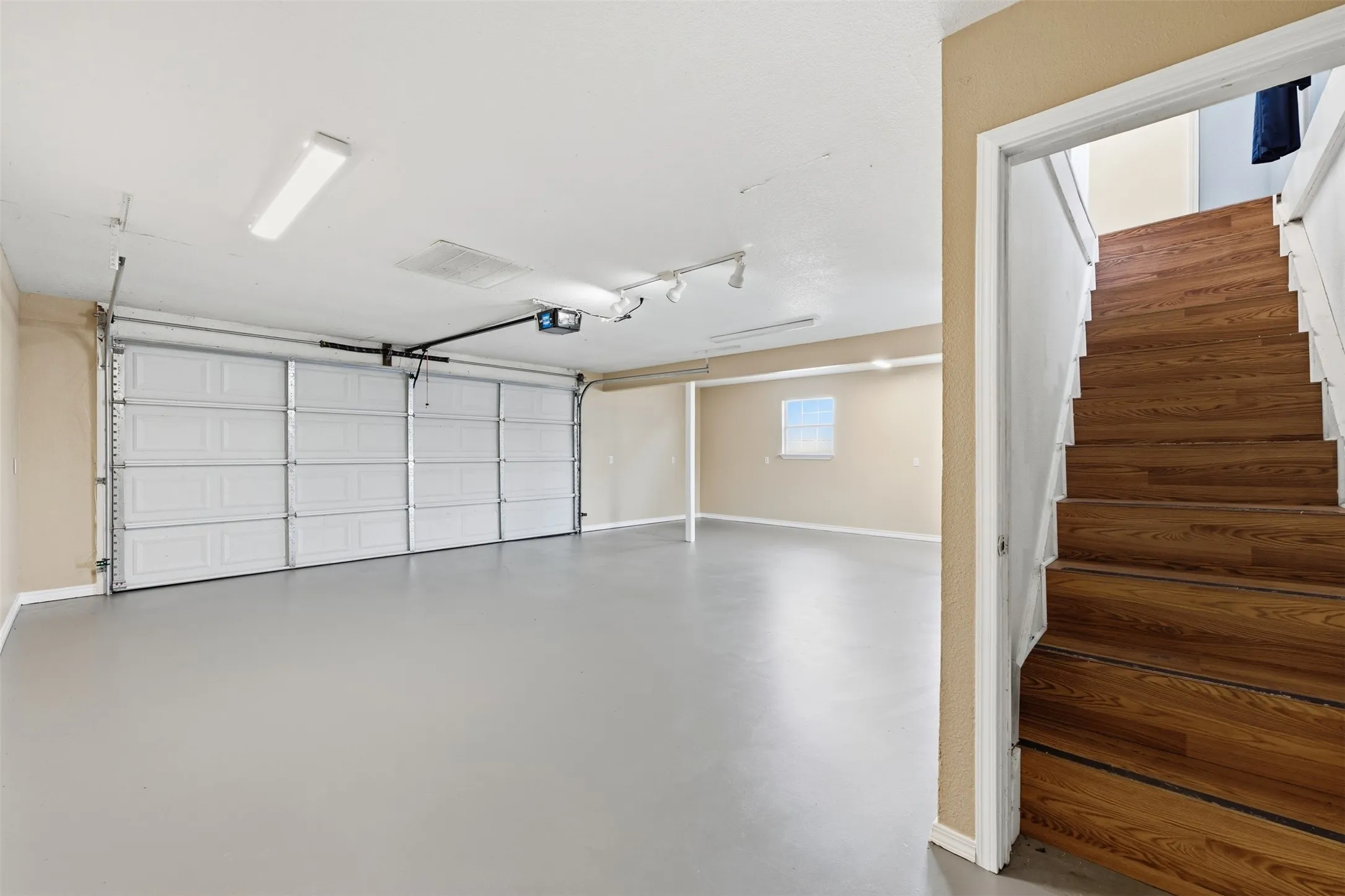 Spacious garage with an automatic overhead door, light gray flooring, and abundant overhead lighting