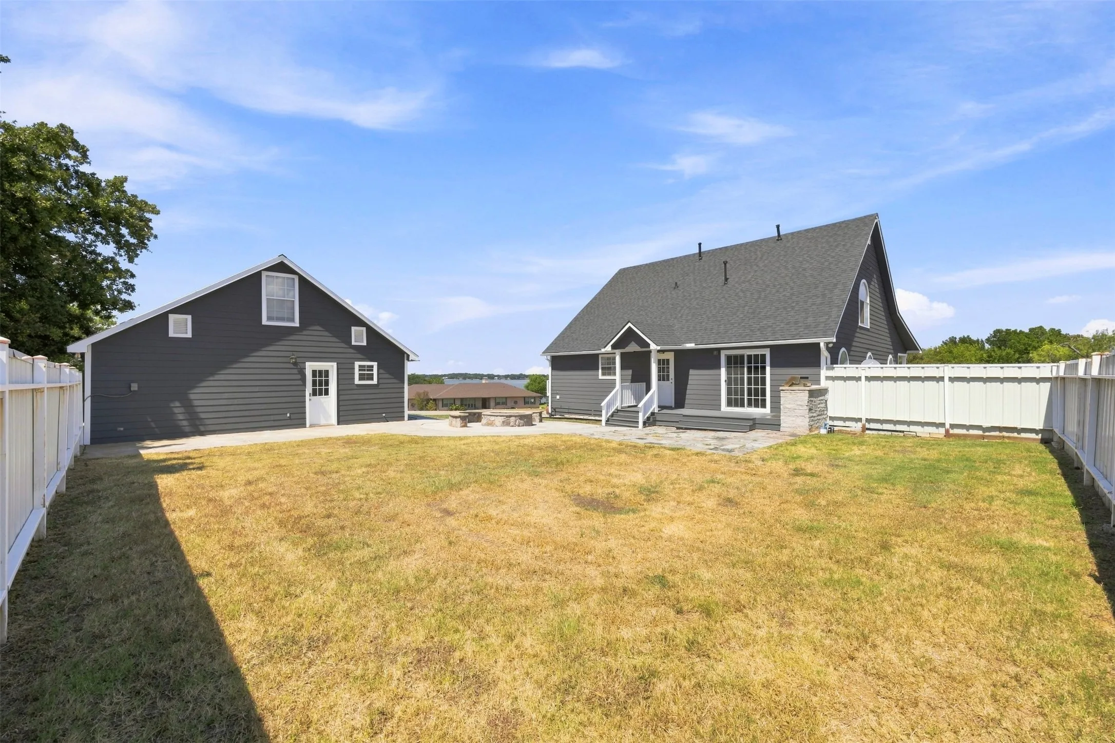 Spacious backyard featuring a large paved patio, a separate accessory building, and a white perimeter fence