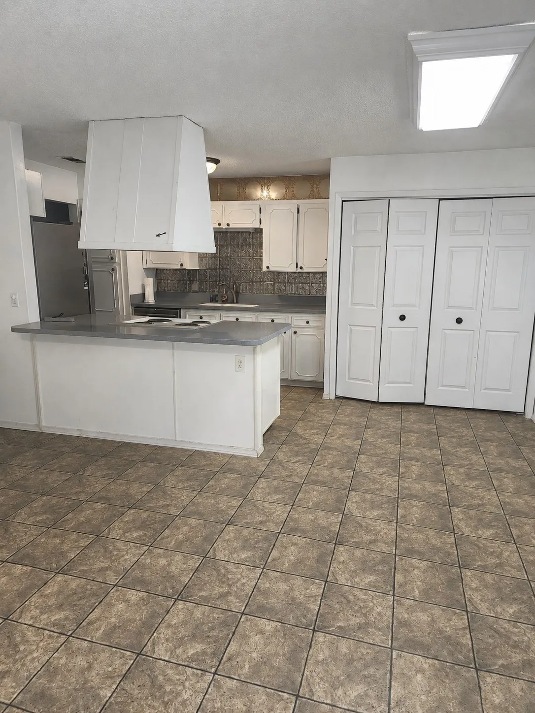 Kitchen featuring an eat-at island with a solid surface countertop, white cabinetry, a tile backsplash, and tile flooring