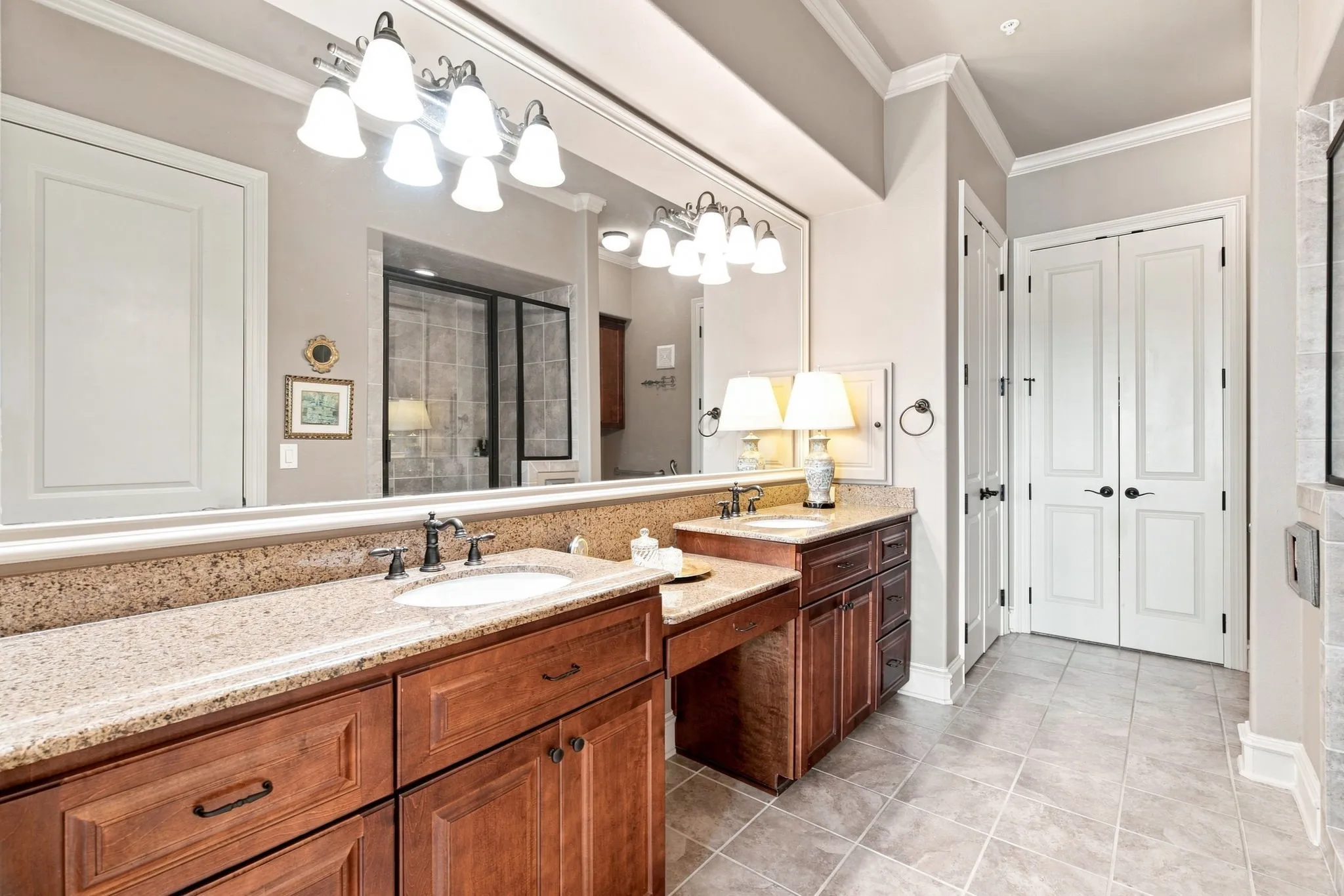 Dual sink vanity with granite countertops, wood-finish cabinetry, and tile flooring