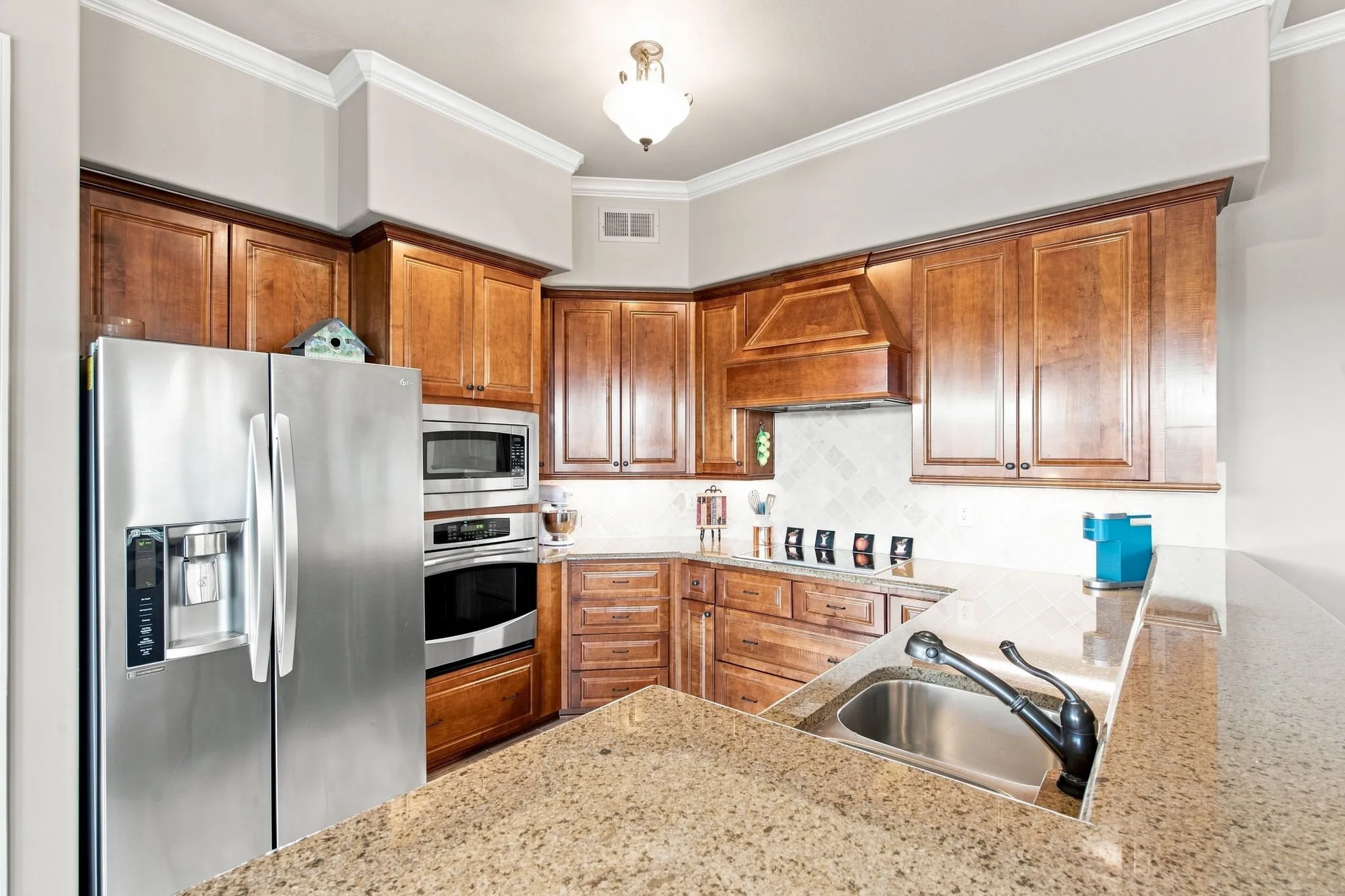 Kitchen featuring wood cabinetry, stainless steel appliances, a built-in oven, a stainless steel sink, and light-toned countertops