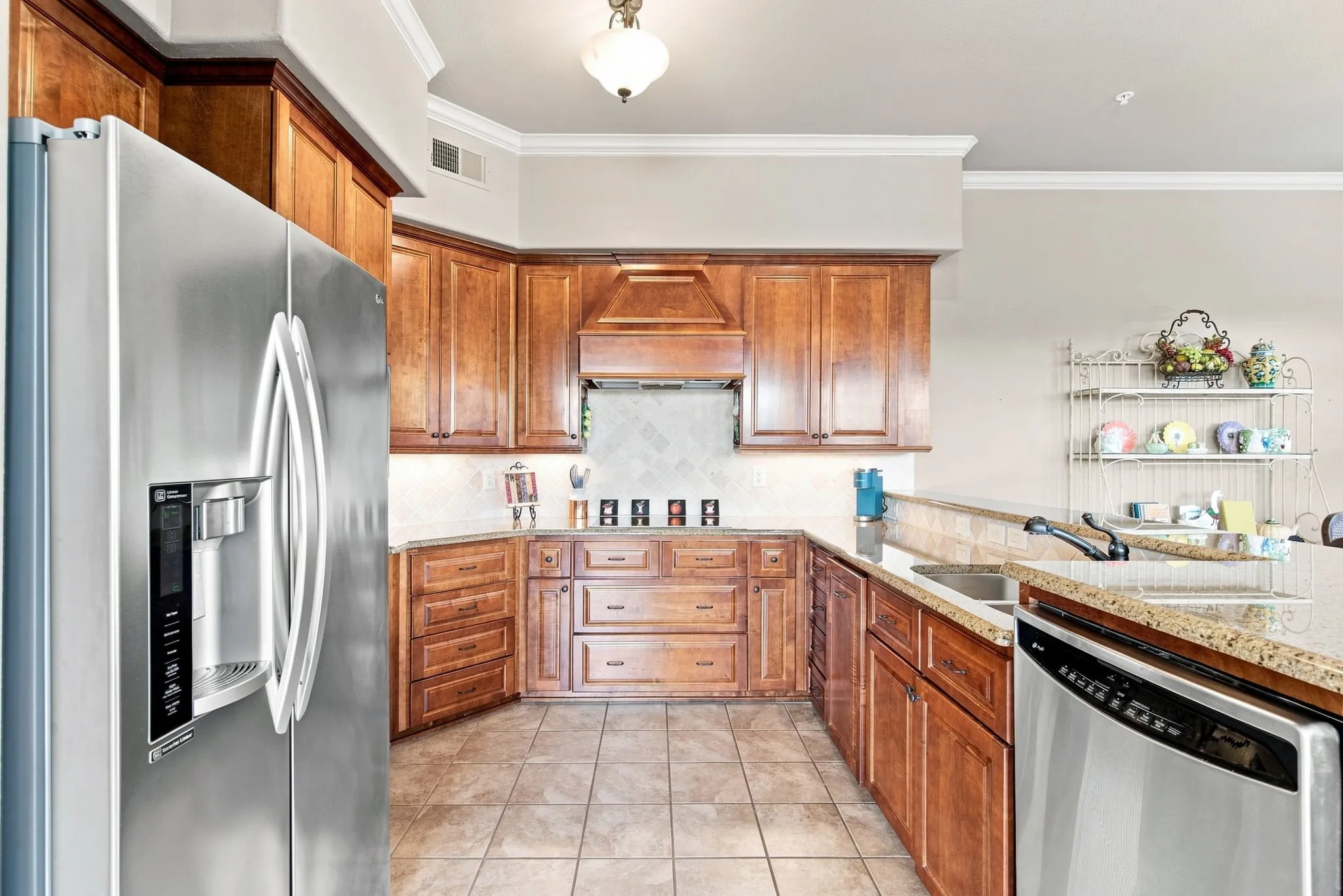 Kitchen featuring wood cabinetry, stainless steel appliances, tile flooring, stone countertops, and crown molding