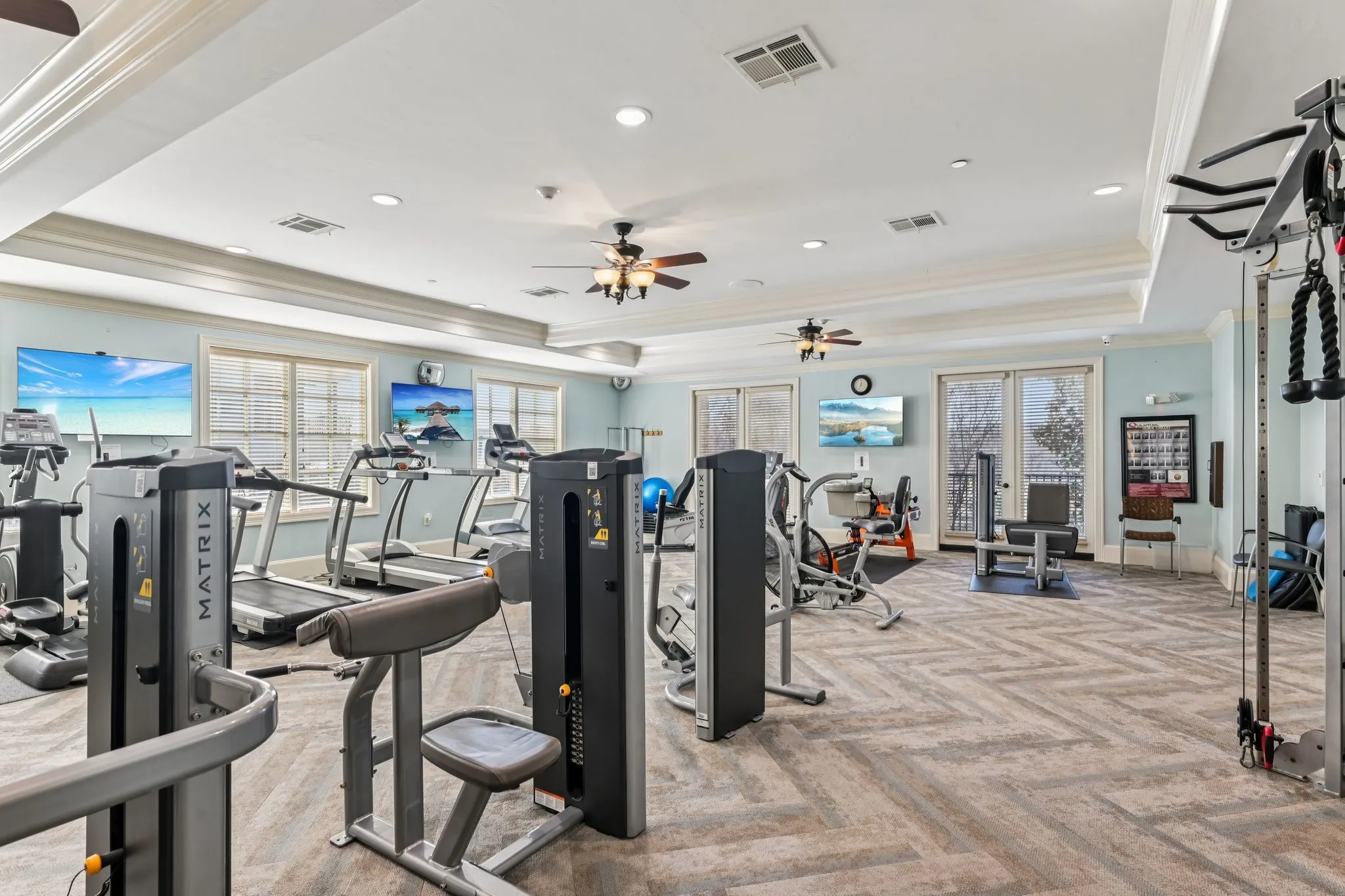 Spacious fitness area featuring herringbone pattern carpet, multiple windows, ceiling fans, and recessed lighting