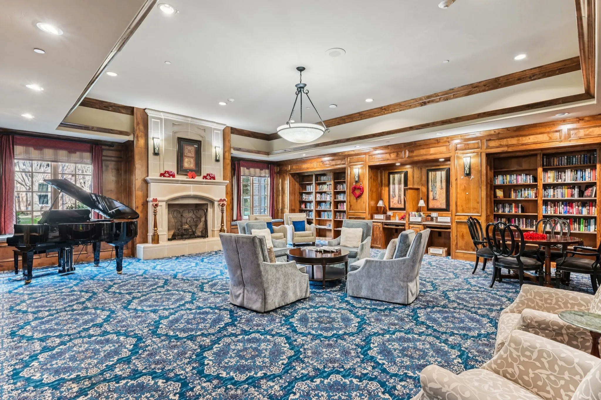 Community library and entertainment space featuring rich wood-paneled walls, built-in cabinetry and bookshelves, fireplace,  and pendant lighting.
