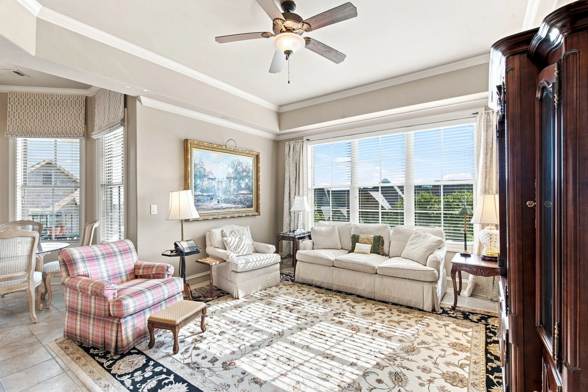 Tray ceiling with crown molding, ceiling fan with integrated lighting, large windows with blinds, tiled flooring, and neutral wall tones