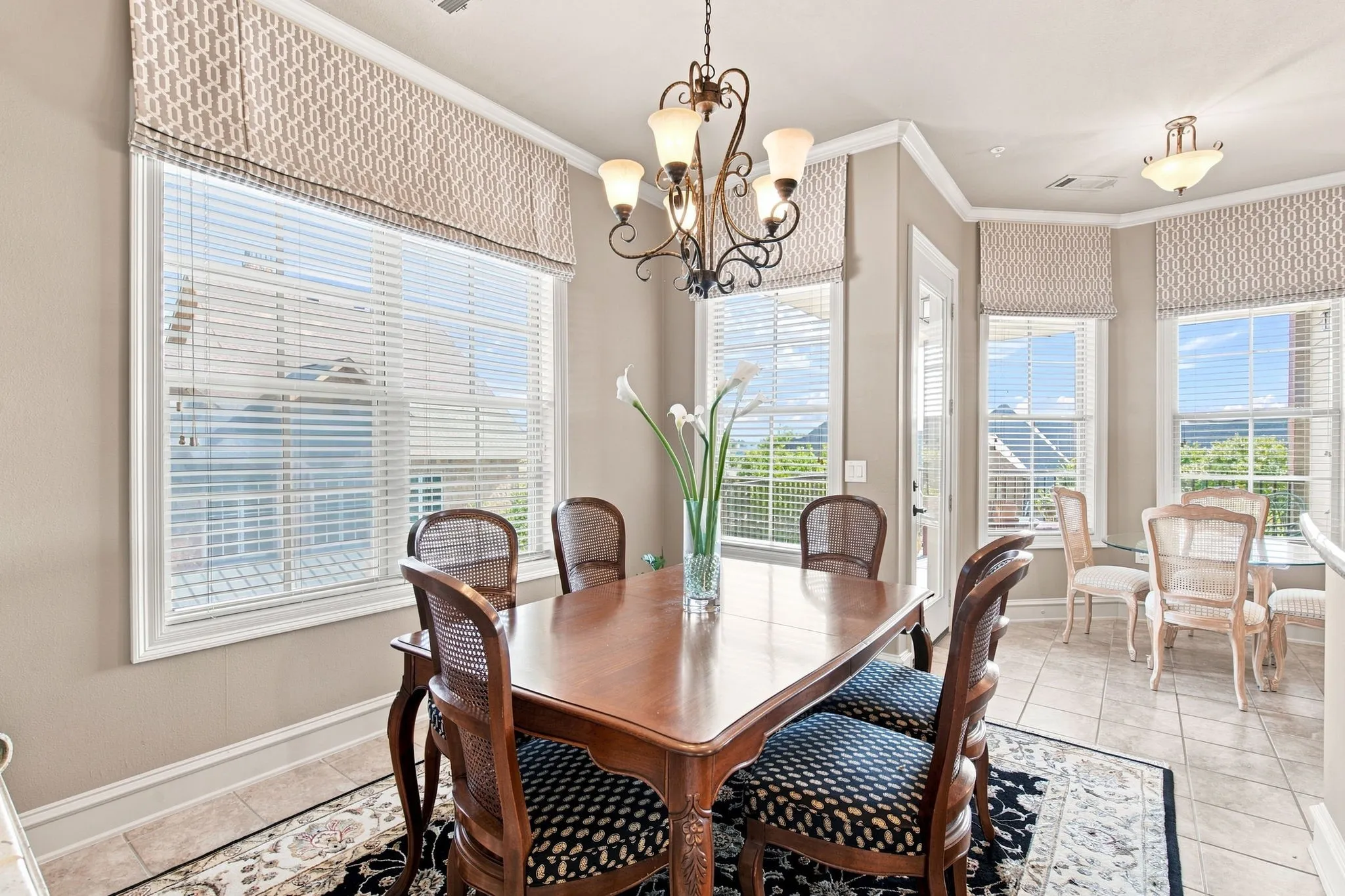 Neutral wall paint, crown molding, patterned window treatments, tile flooring, and a decorative chandelier