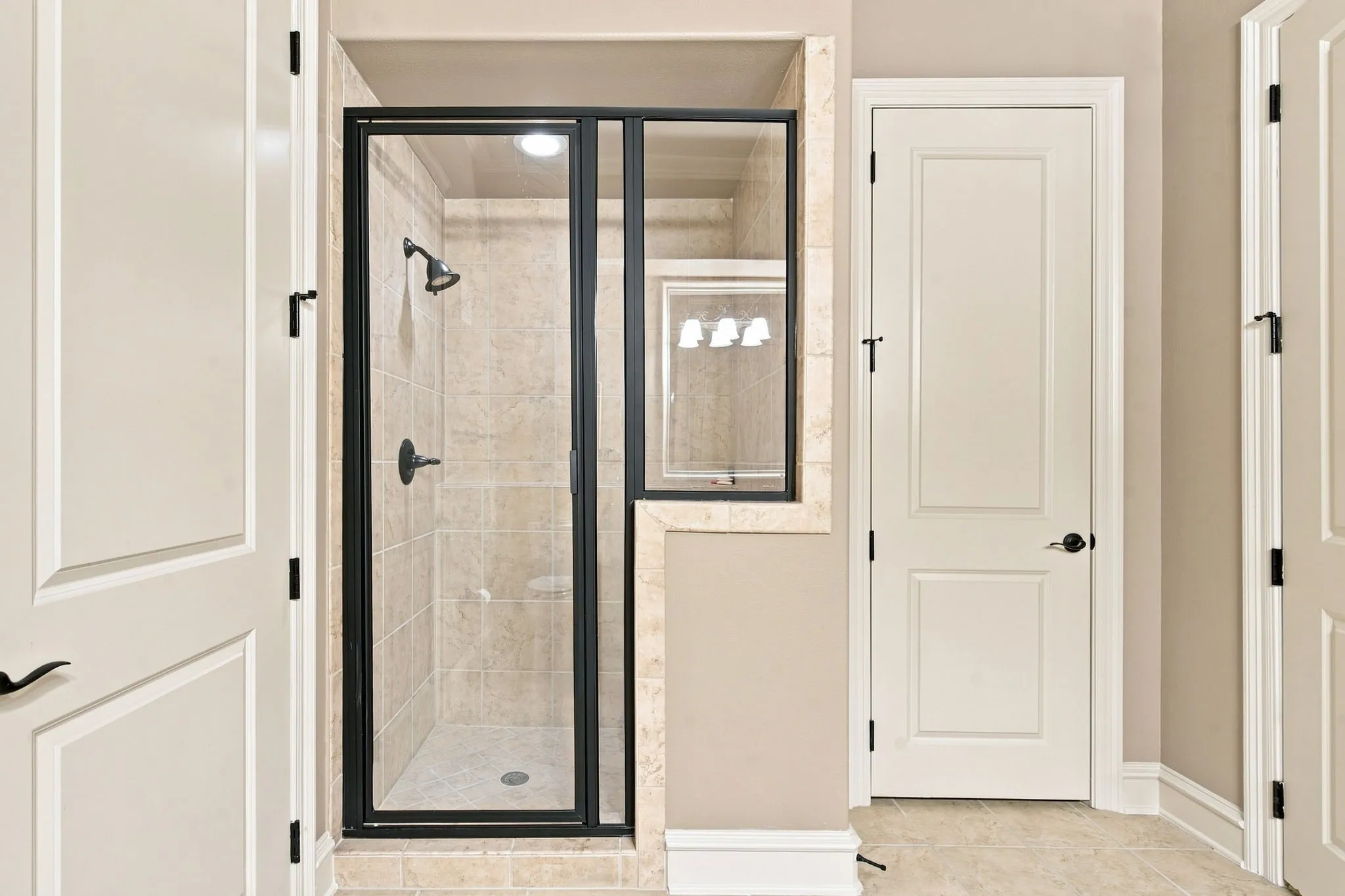 Walk-in shower with clear glass enclosure and black frame, featuring a tiled interior and showerhead