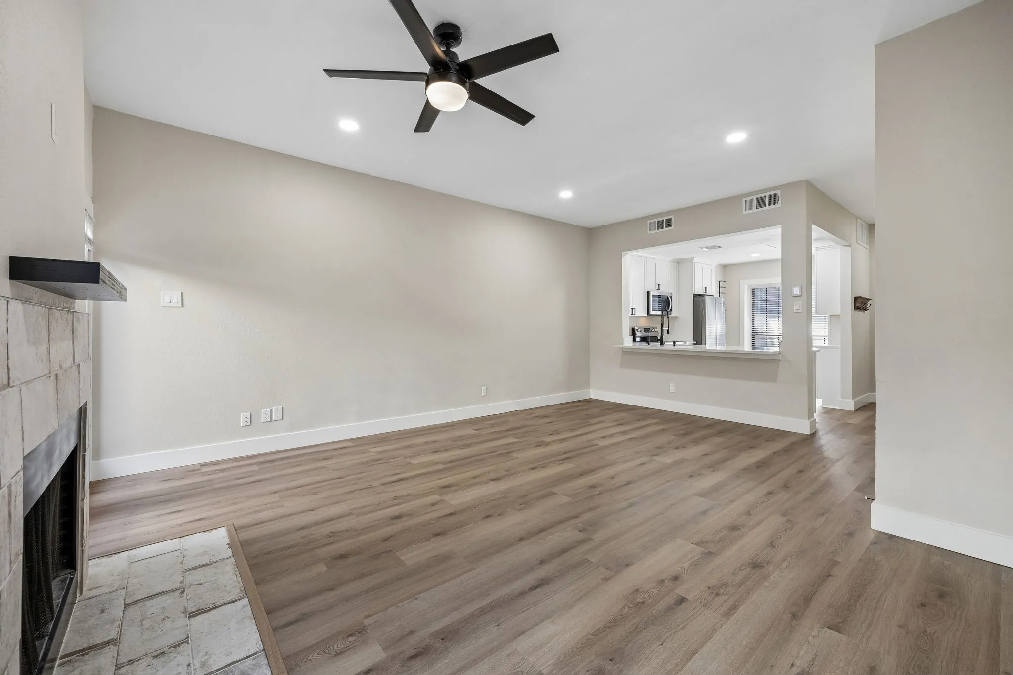 Spacious living area featuring wood-finish flooring, a tiled fireplace with a black mantel, and a ceiling fan with integrated lighting