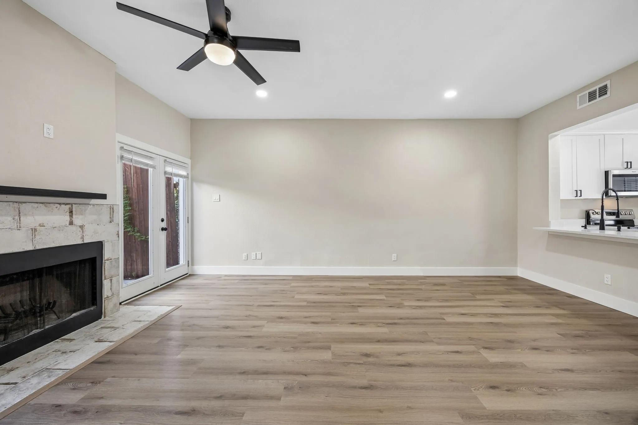 Open-concept living area featuring wood-finish flooring, a stone-clad fireplace with a dark mantel, and recessed lighting