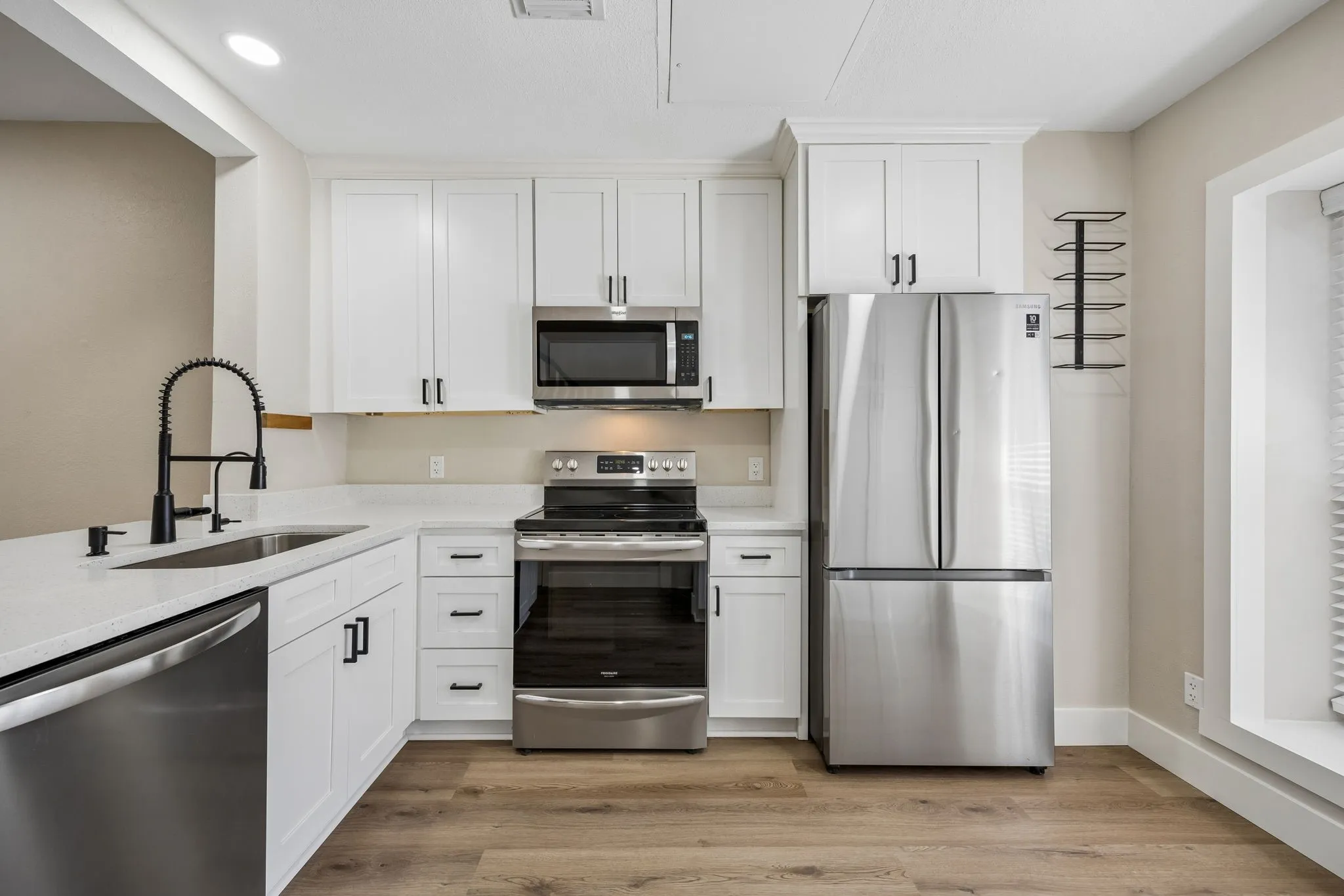 Modern kitchen featuring white shaker cabinetry, stainless steel appliances, light-toned countertops, a matte black faucet, and wood-finish flooring