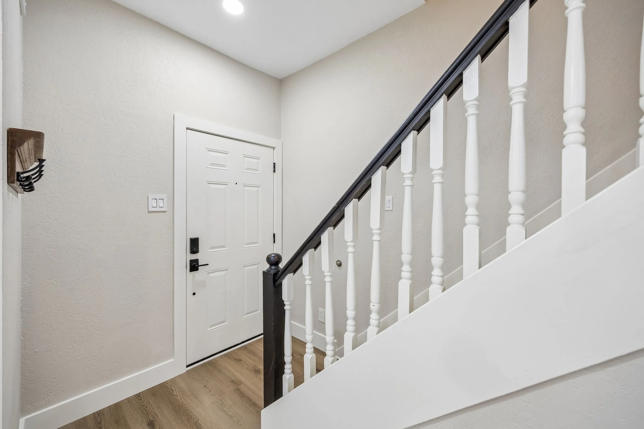 Entryway featuring wood-finish flooring, a white paneled door with matte black hardware, and a staircase with white spindles and a dark wood handrail