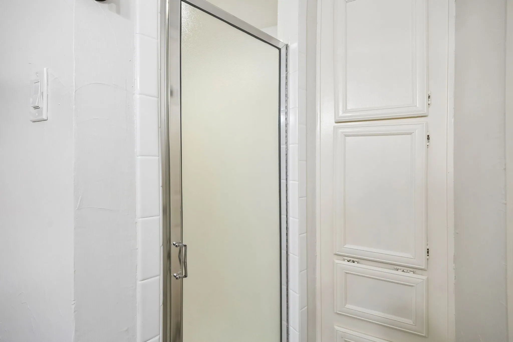 Frosted glass shower enclosure with chrome hardware, white subway tile surround, and built-in white paneled cabinetry