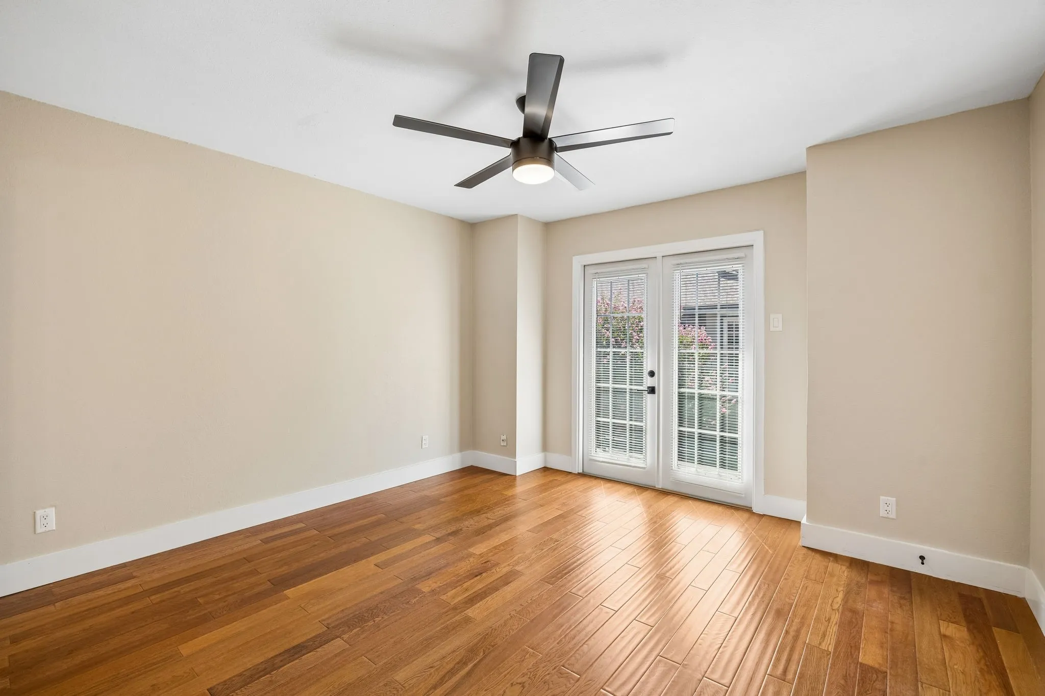 Spacious room featuring wood-finish flooring, light-toned walls, and a modern ceiling fan