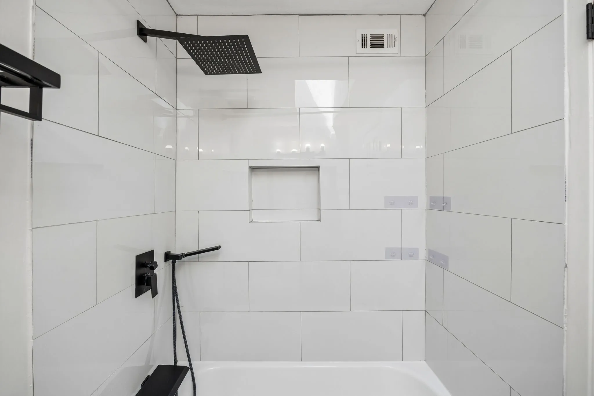 Shower enclosure featuring white subway tile surround, a built-in shower niche, and a matte black rainfall showerhead