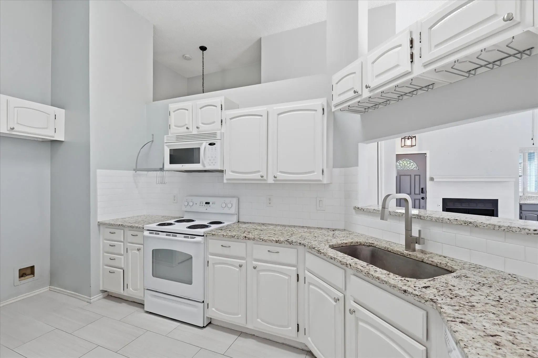 Kitchen featuring white cabinetry, light-toned granite countertops, white subway tile backsplash, and a stainless steel sink with a gooseneck faucet