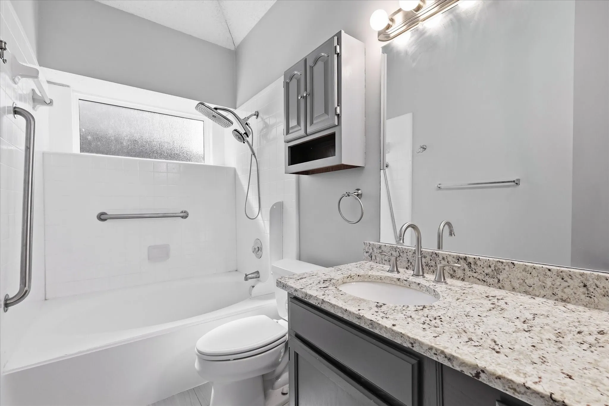 White bathtub with a frosted window, chrome grab bars, and a multi-function showerhead