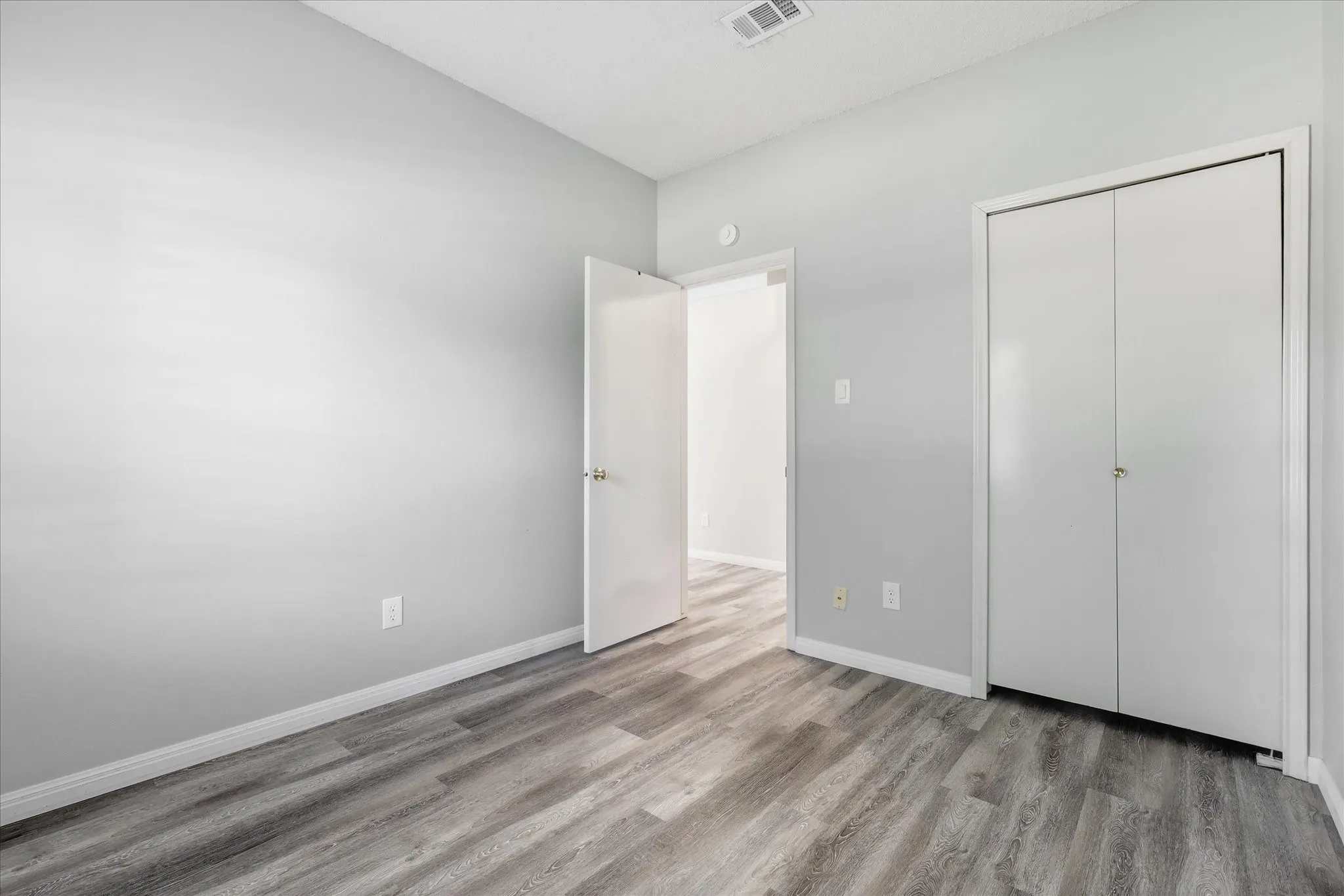 Wood-finish flooring, light gray wall paint, white trim, and bi-fold closet doors
