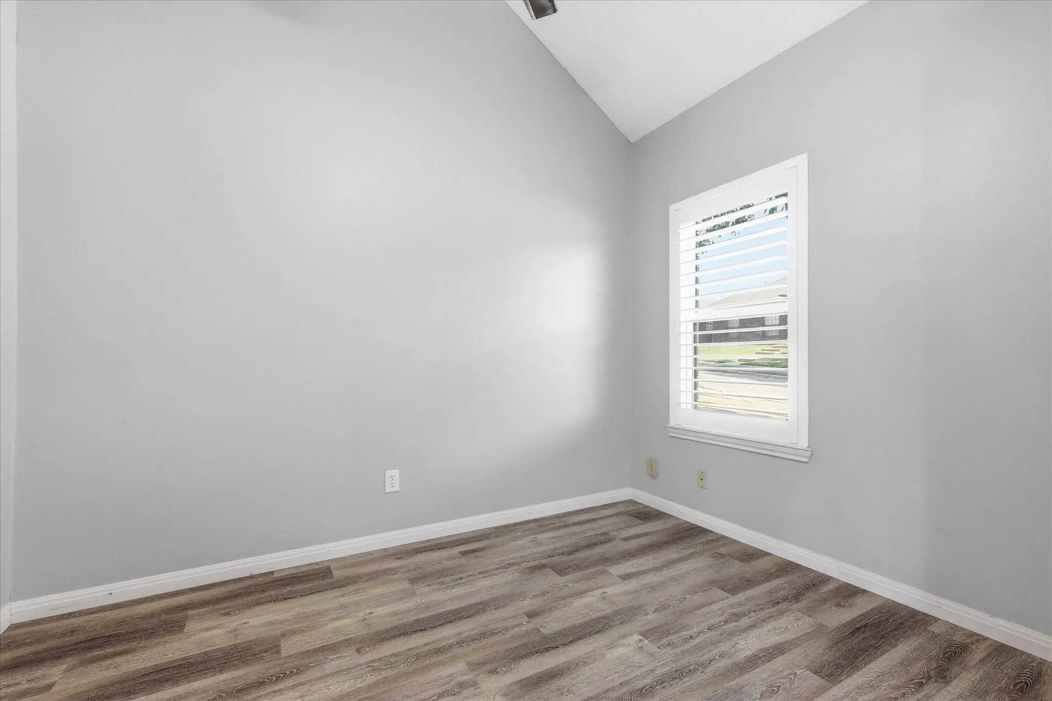 Vaulted ceiling, wood-finish flooring, white plantation shutters, and a single window