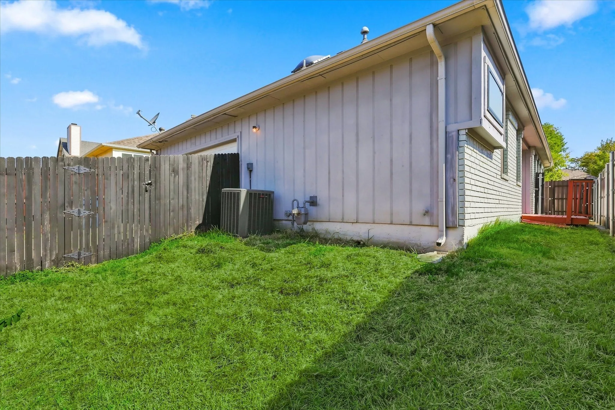 Side exterior with a privacy fence, two exterior units, a small deck, and a bay window