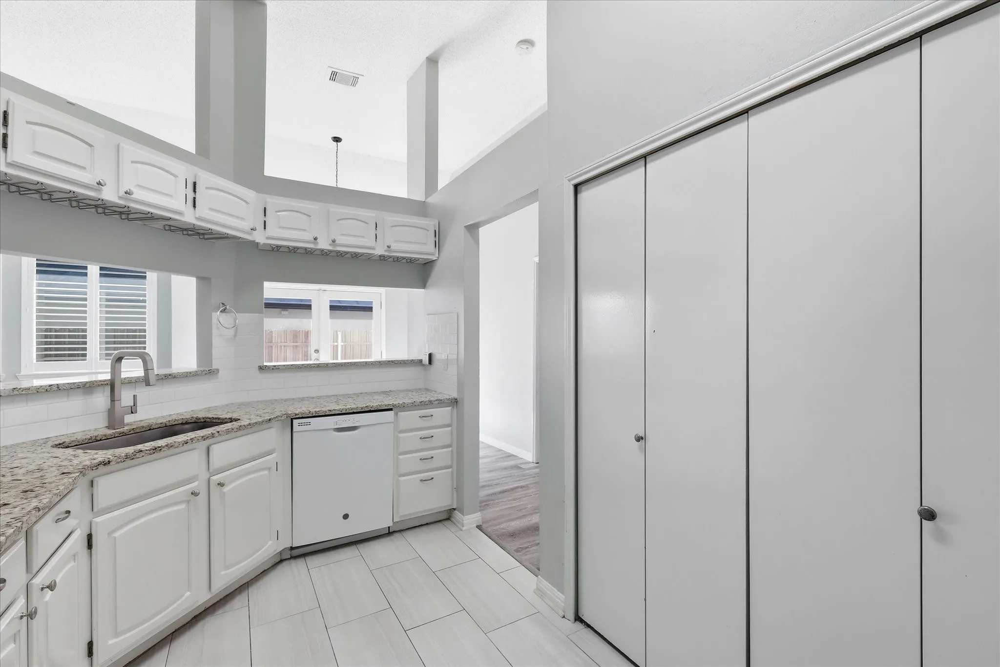 Kitchen featuring white cabinetry, light-toned granite countertops, a white subway tile backsplash, and a stainless steel sink with a gooseneck faucet