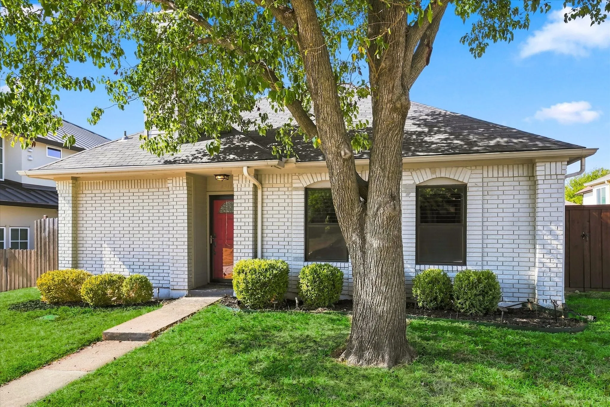 White brick exterior with a red front door, featuring arched windows, dark roofing, and a manicured lawn