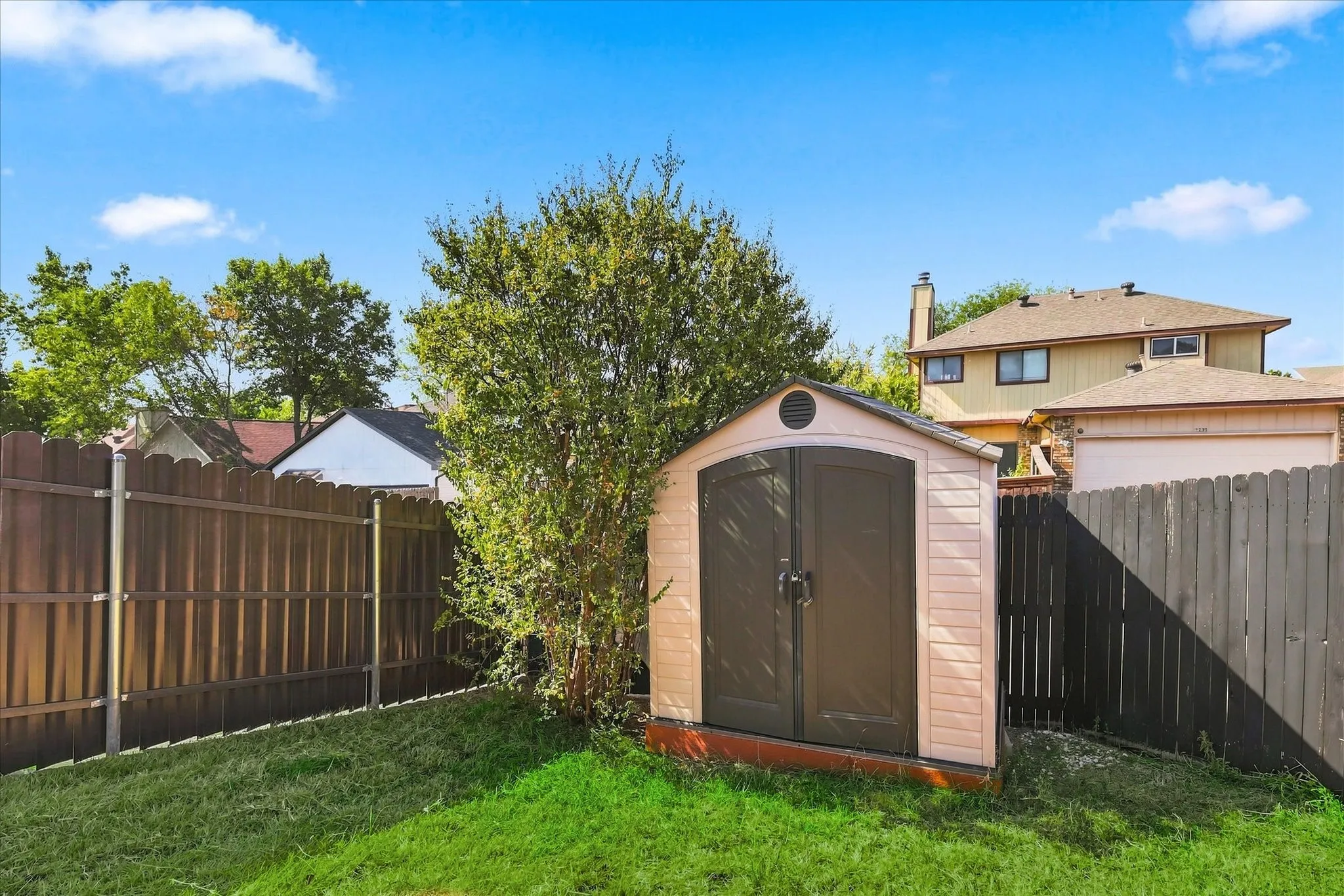 Expansive green lawn with a storage shed featuring double doors and an arched top, bordered by a privacy fence