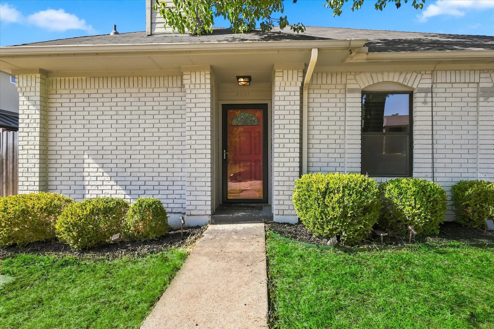 White brick exterior with a red front door, featuring an arched window and a walkway