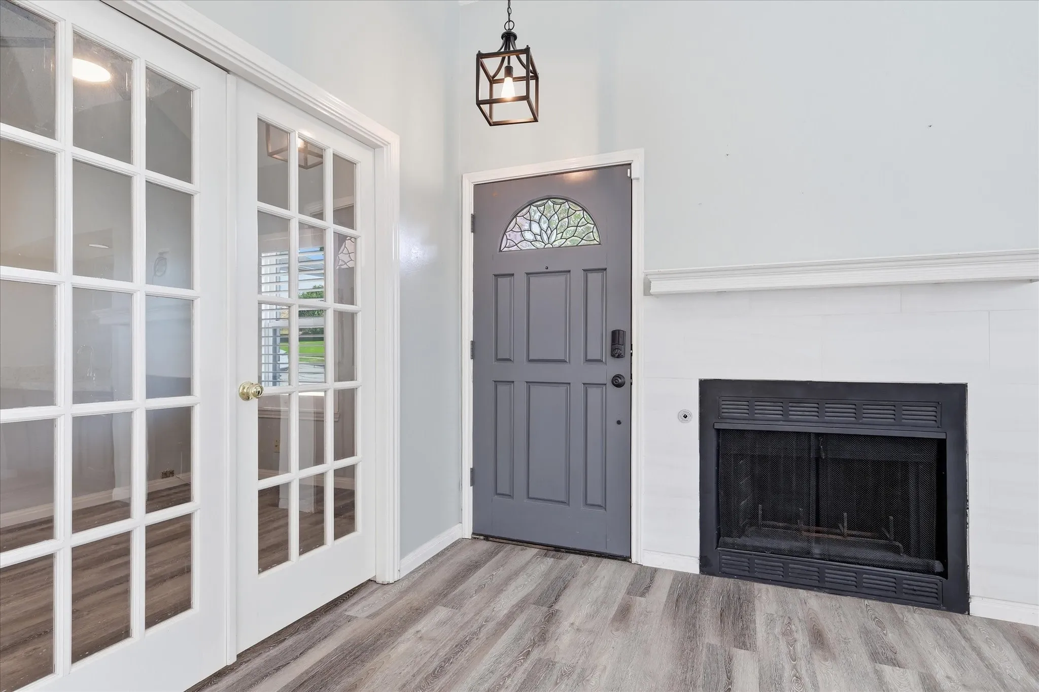 Entryway featuring wood-finish flooring, a fireplace with a white mantel, and a gray front door with decorative glass