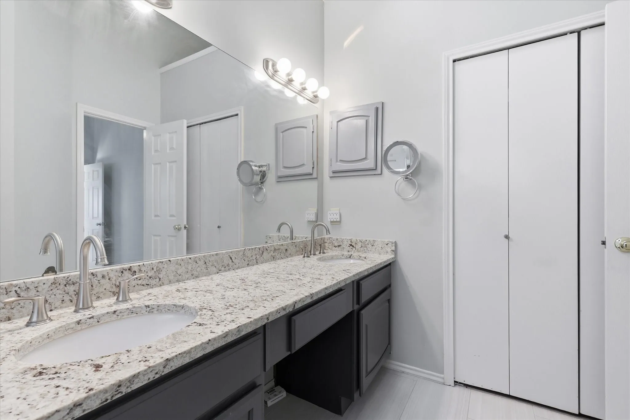 Dual sinks set into a granite-look countertop with a full-width mirror and dark cabinetry