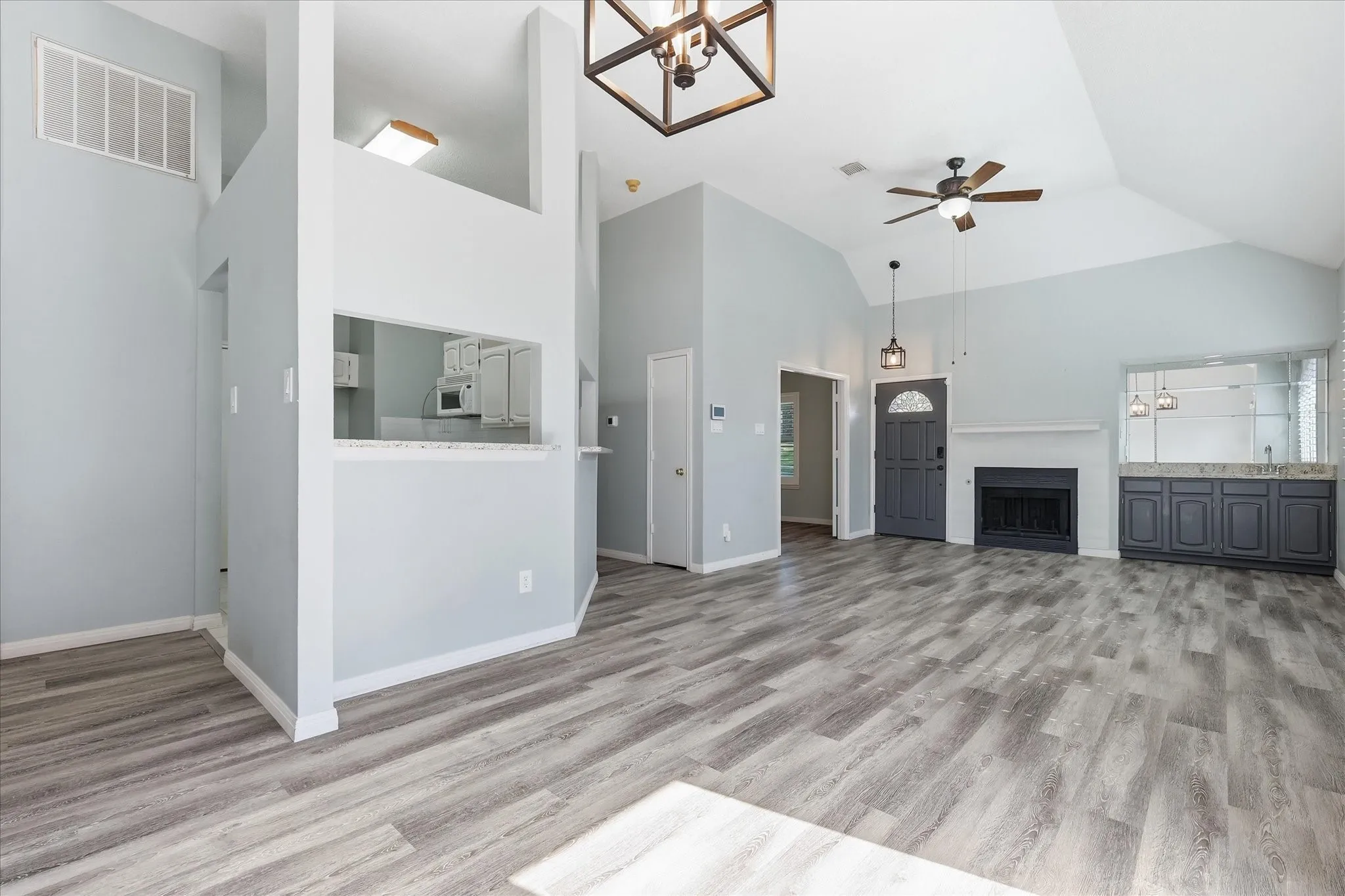 Vaulted ceiling with a ceiling fan, wood-finish flooring, fireplace with a mantel, built-in cabinetry with a countertop, and a built-in shelf