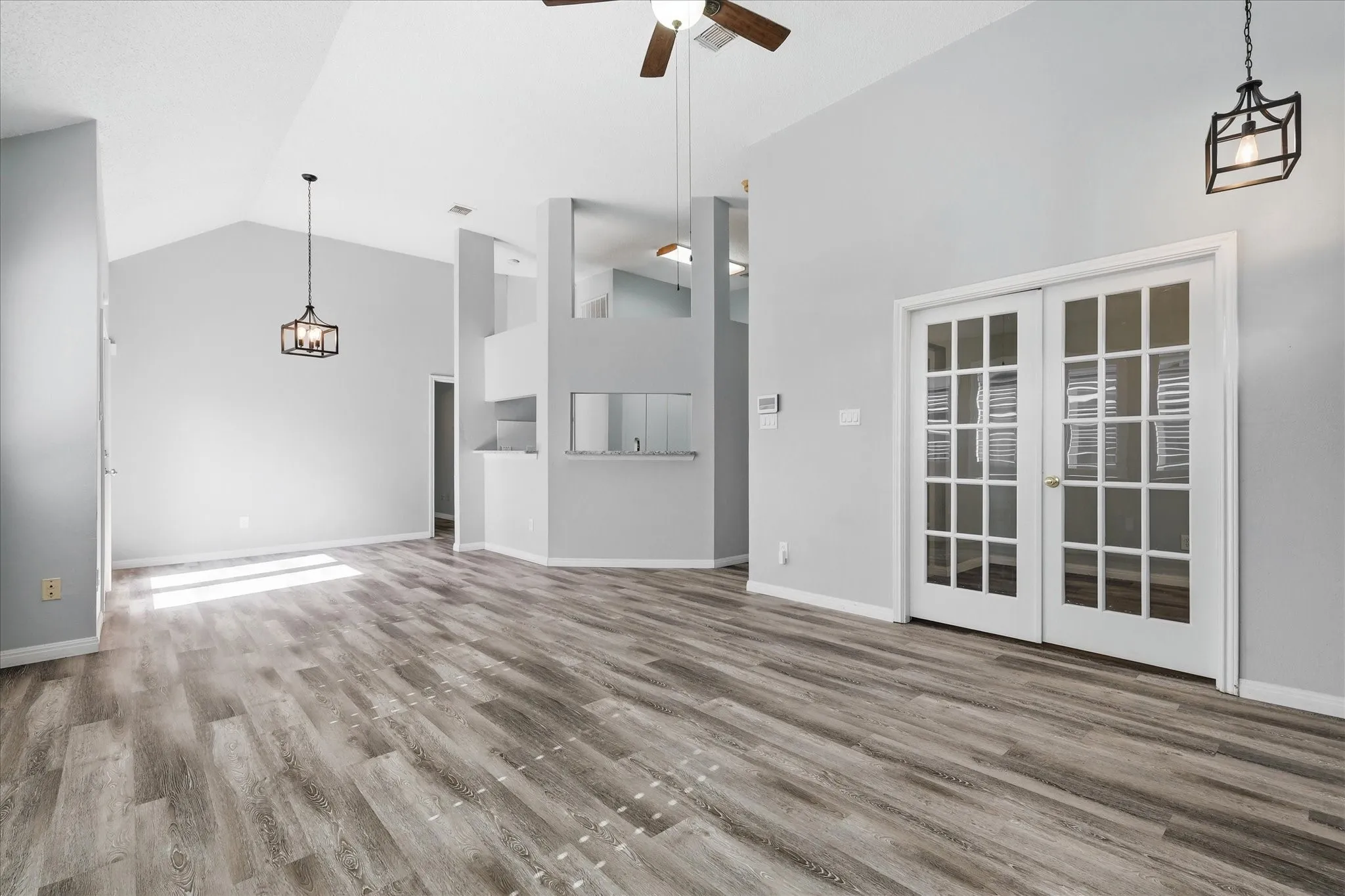 Vaulted ceilings, wood-finish flooring, white French doors, and contemporary pendant lighting