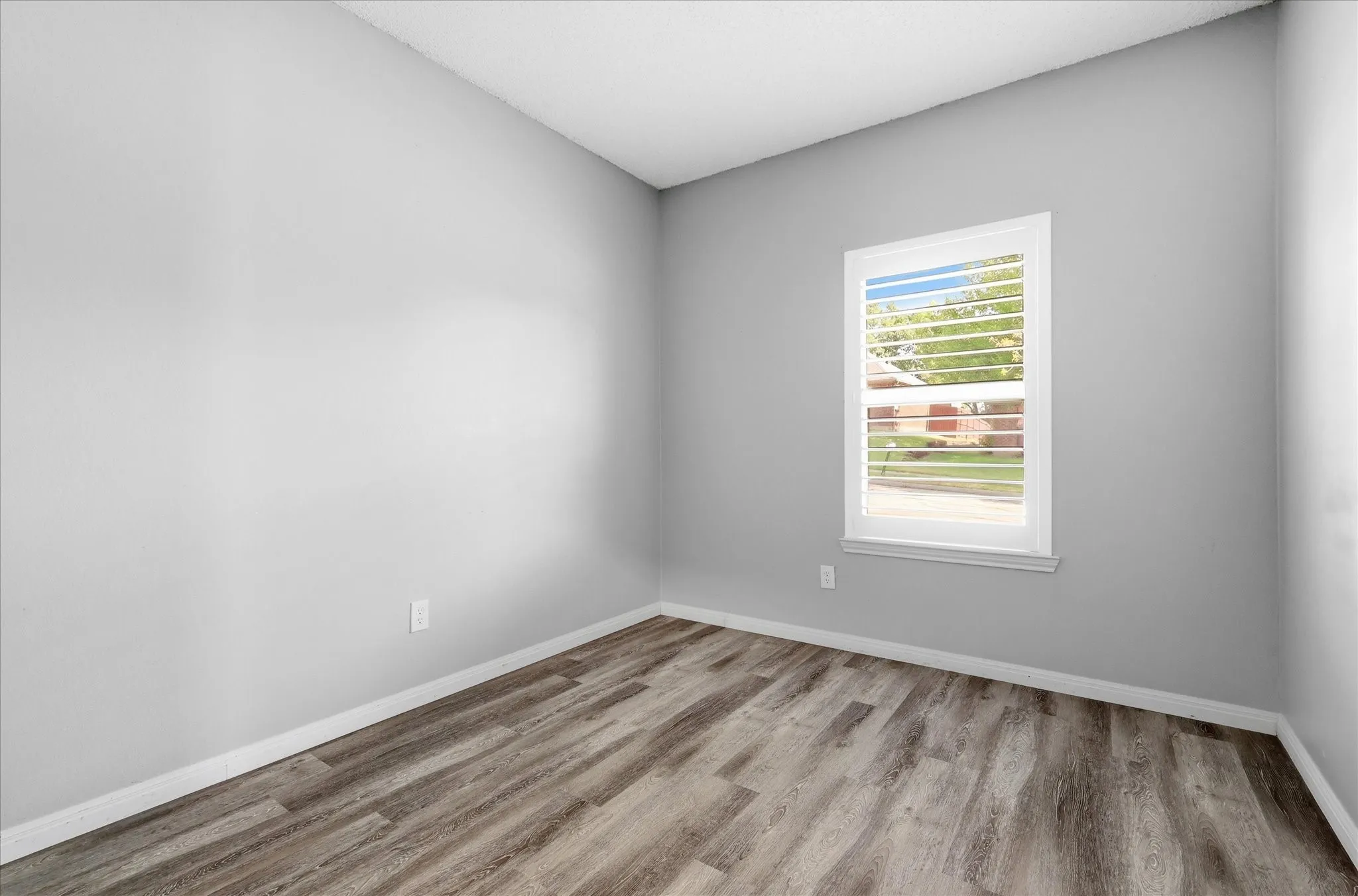 Wood-finish flooring, light grey wall paint, and a double-pane window with white framing