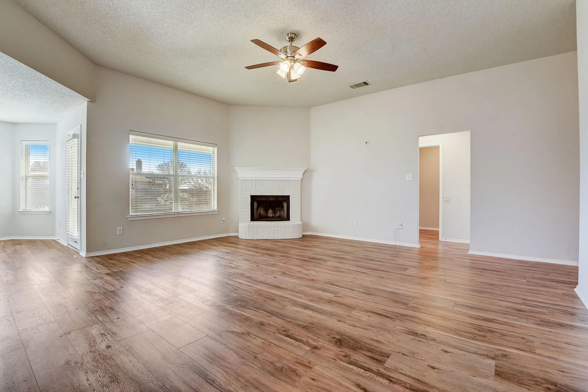 Unfurnished living room featuring light wood-type flooring, visible vents, a fireplace, and ceiling fan