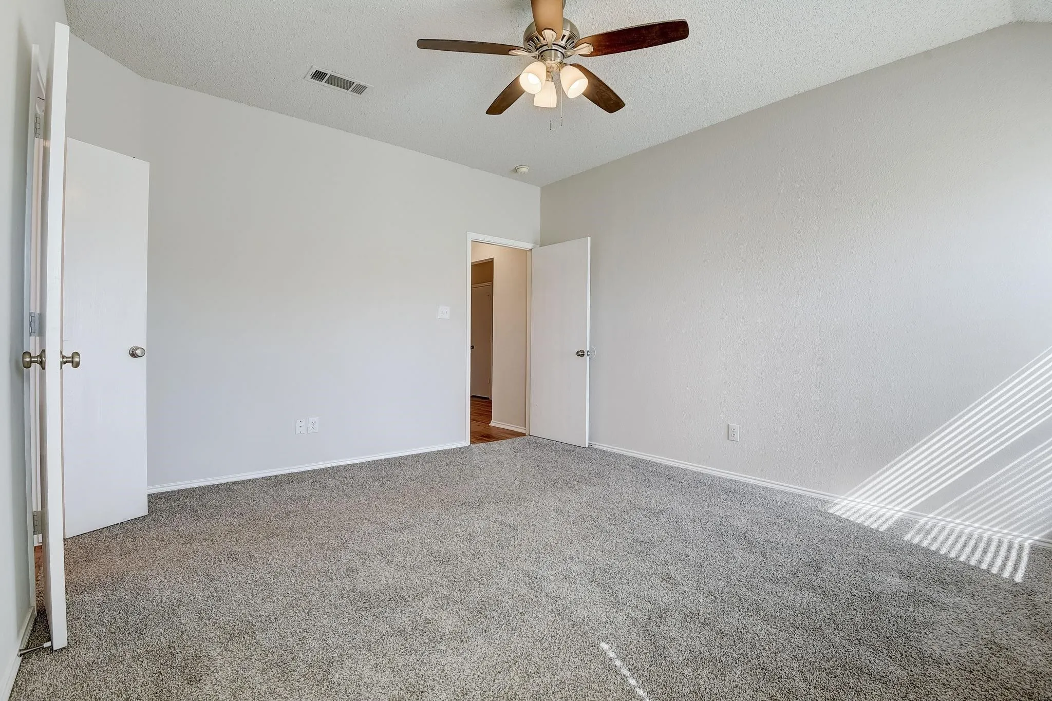 Unfurnished bedroom featuring visible vents, baseboards, a ceiling fan, carpet, and a textured ceiling