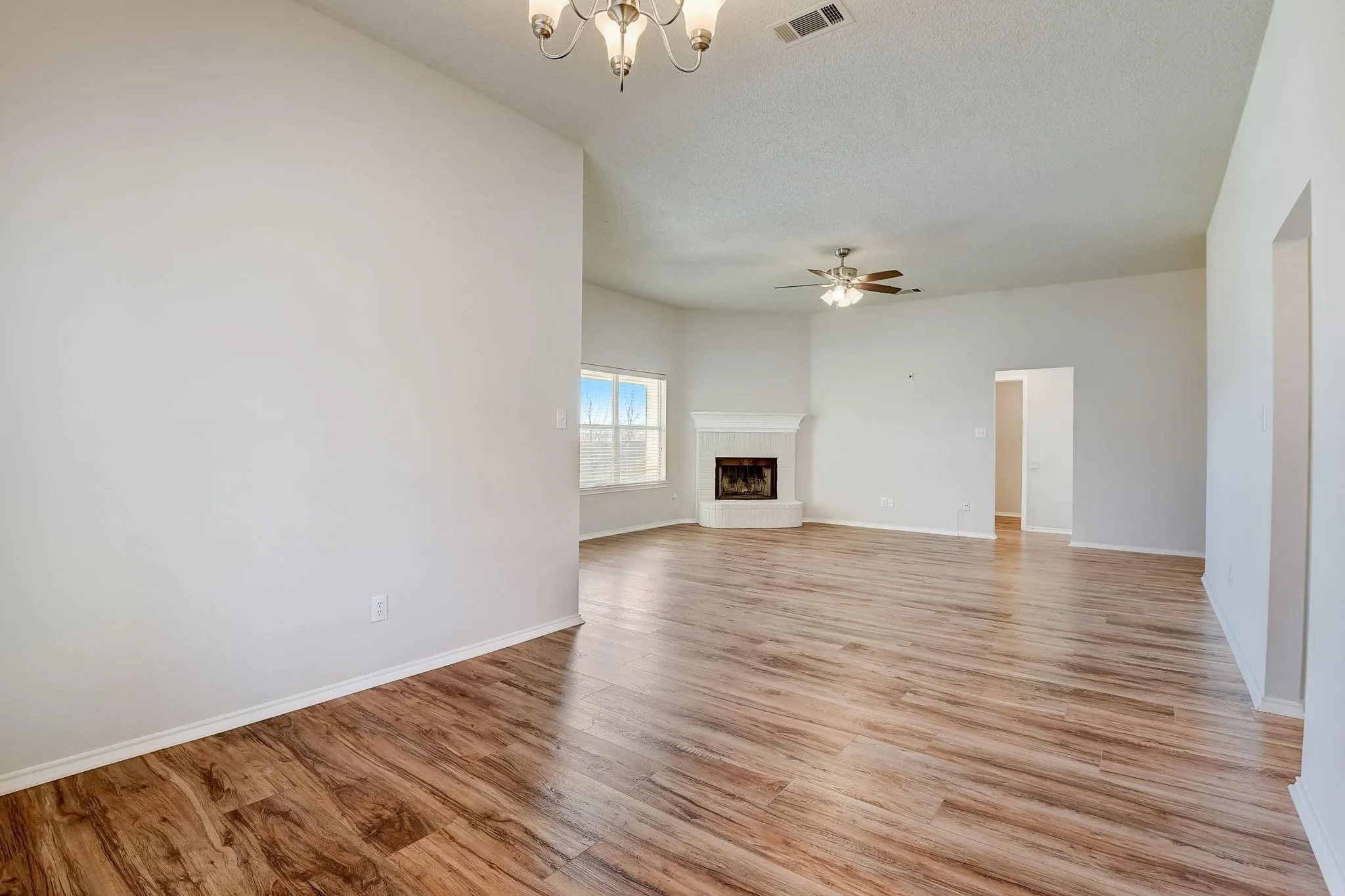 Unfurnished living room featuring light wood finished floors, baseboards, visible vents, a fireplace with raised hearth, and ceiling fan with notable chandelier
