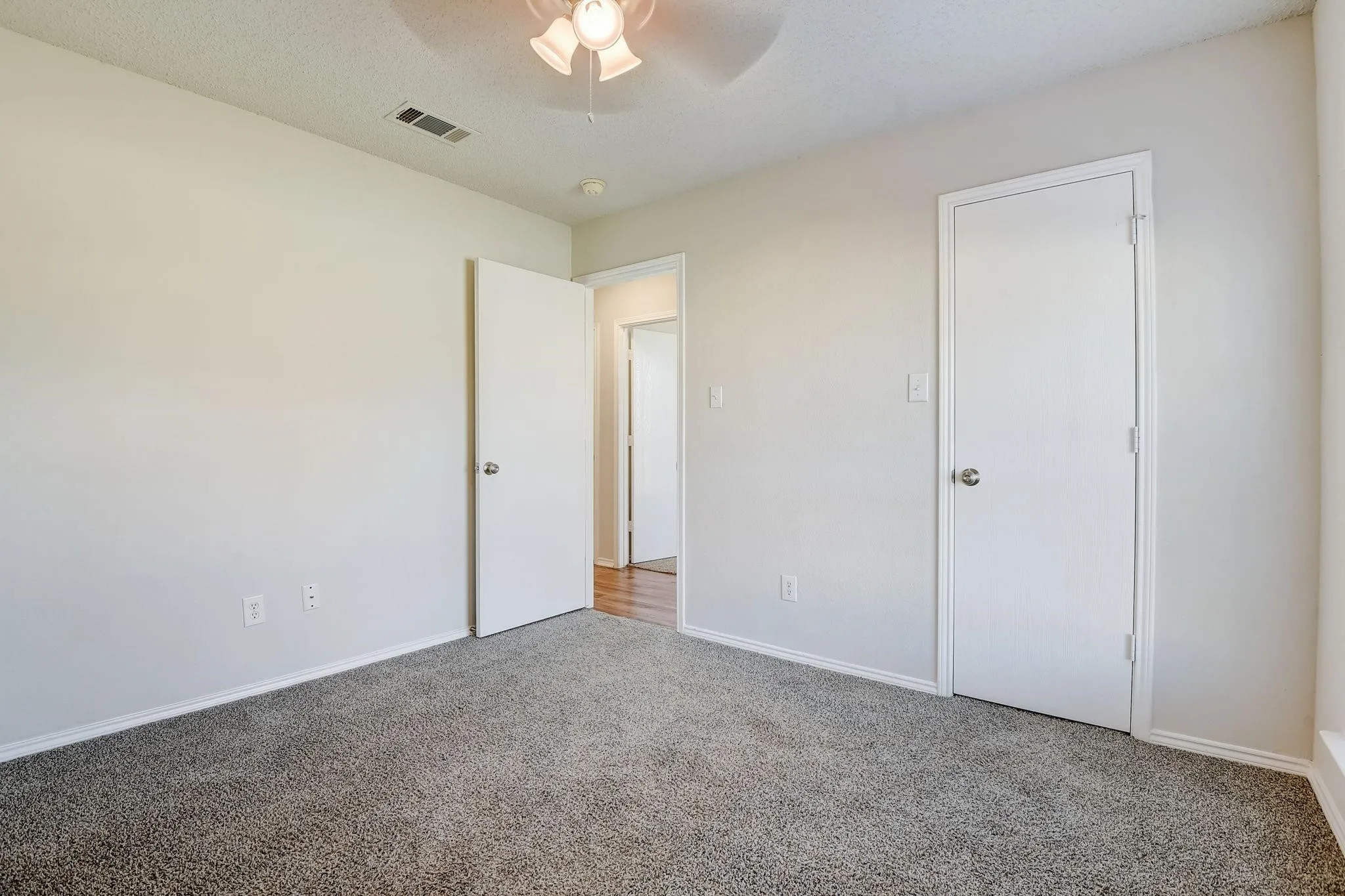 Unfurnished bedroom featuring a textured ceiling, a ceiling fan, visible vents, baseboards, and carpet