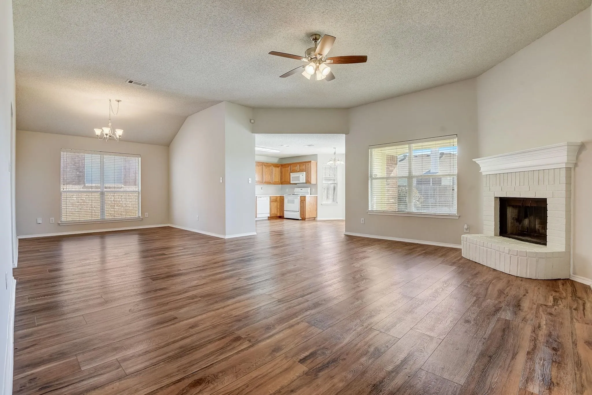 Unfurnished living room featuring dark wood-style floors, ceiling fan with notable chandelier, a fireplace, and plenty of natural light
