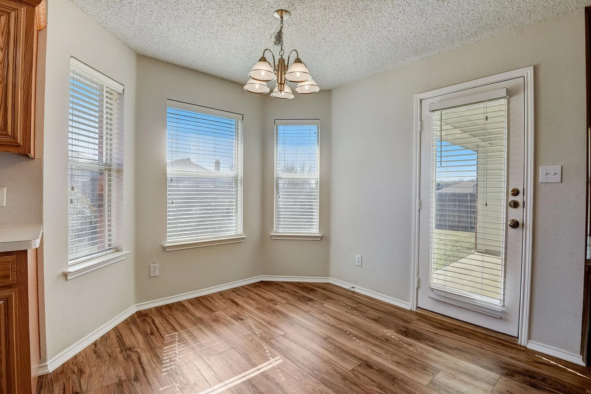 Unfurnished dining area with light wood-type flooring, a notable chandelier, a textured ceiling, and baseboards