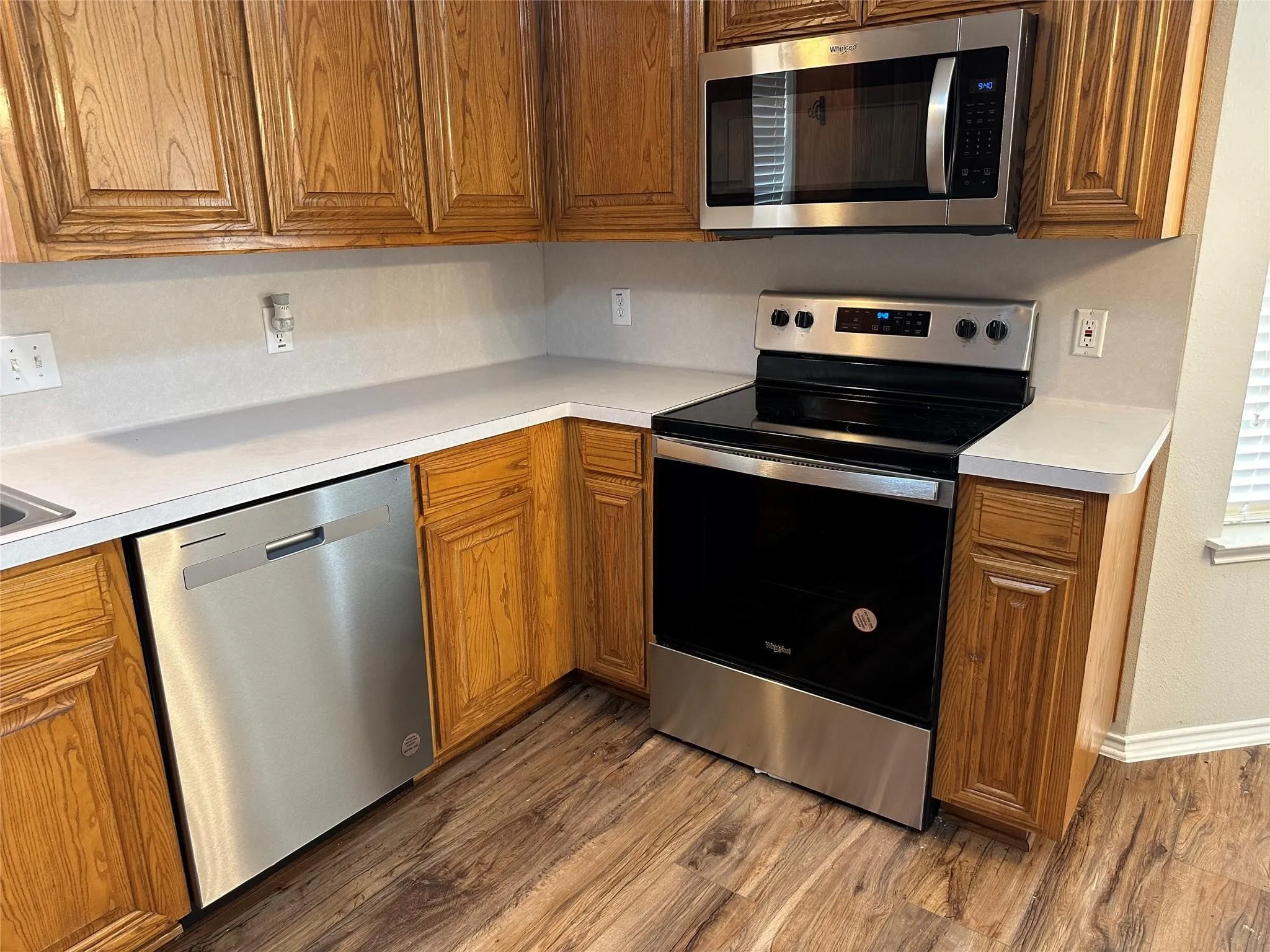 Kitchen featuring light countertops, appliances with stainless steel finishes, brown cabinetry, and wood finished floors