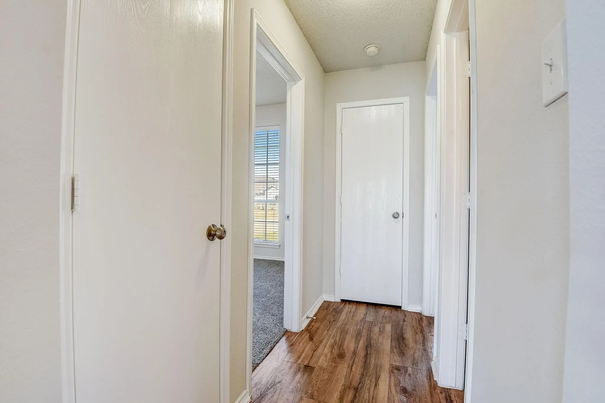 Corridor with a textured ceiling, baseboards, and wood finished floors